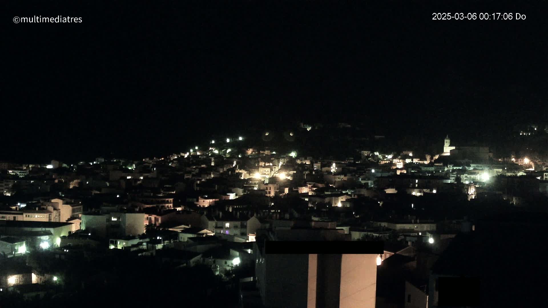 A nighttime, aerial view of a town nestled on a hillside, illuminated by scattered lights.
