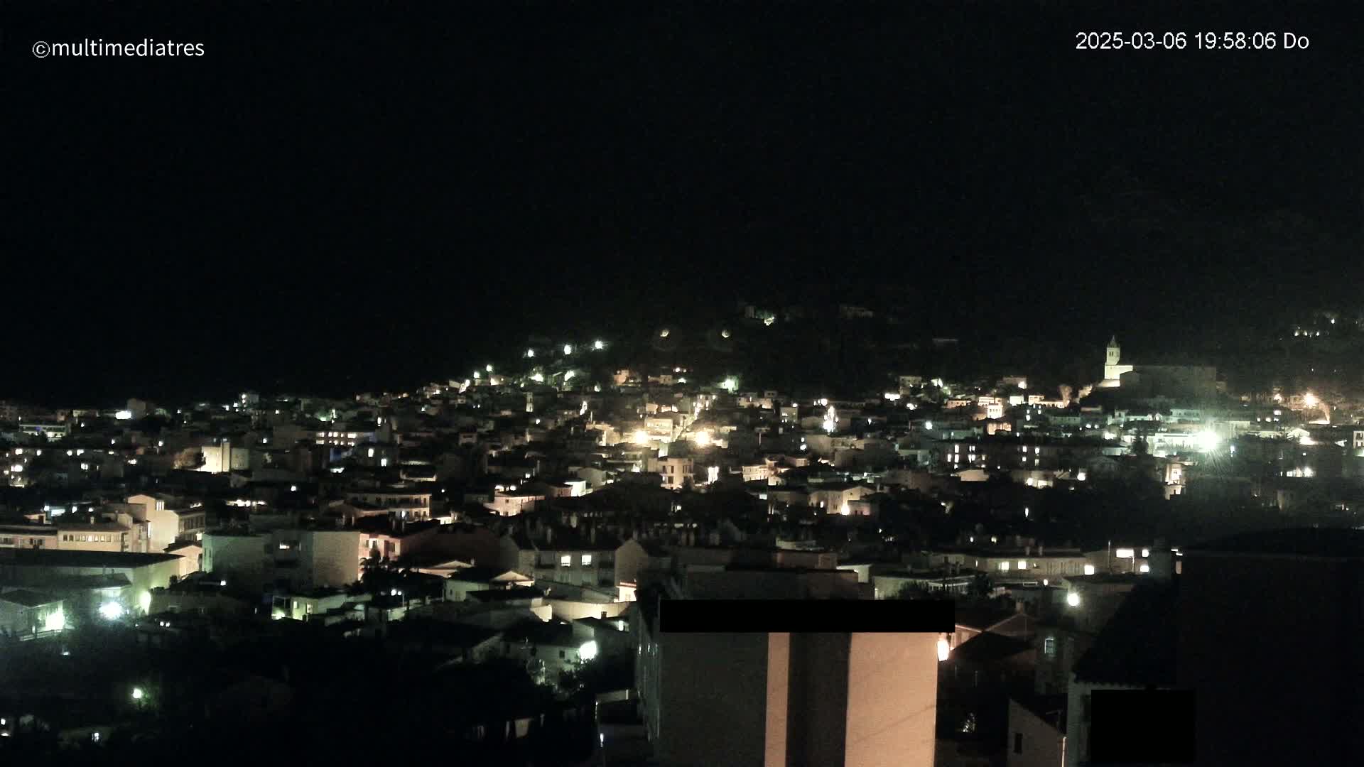 A nighttime view of a town nestled on a hill, illuminated by the lights of numerous buildings.