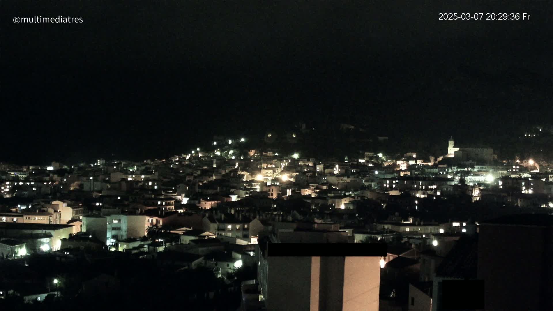 A nighttime view of a town illuminated by scattered lights under a dark, overcast sky.