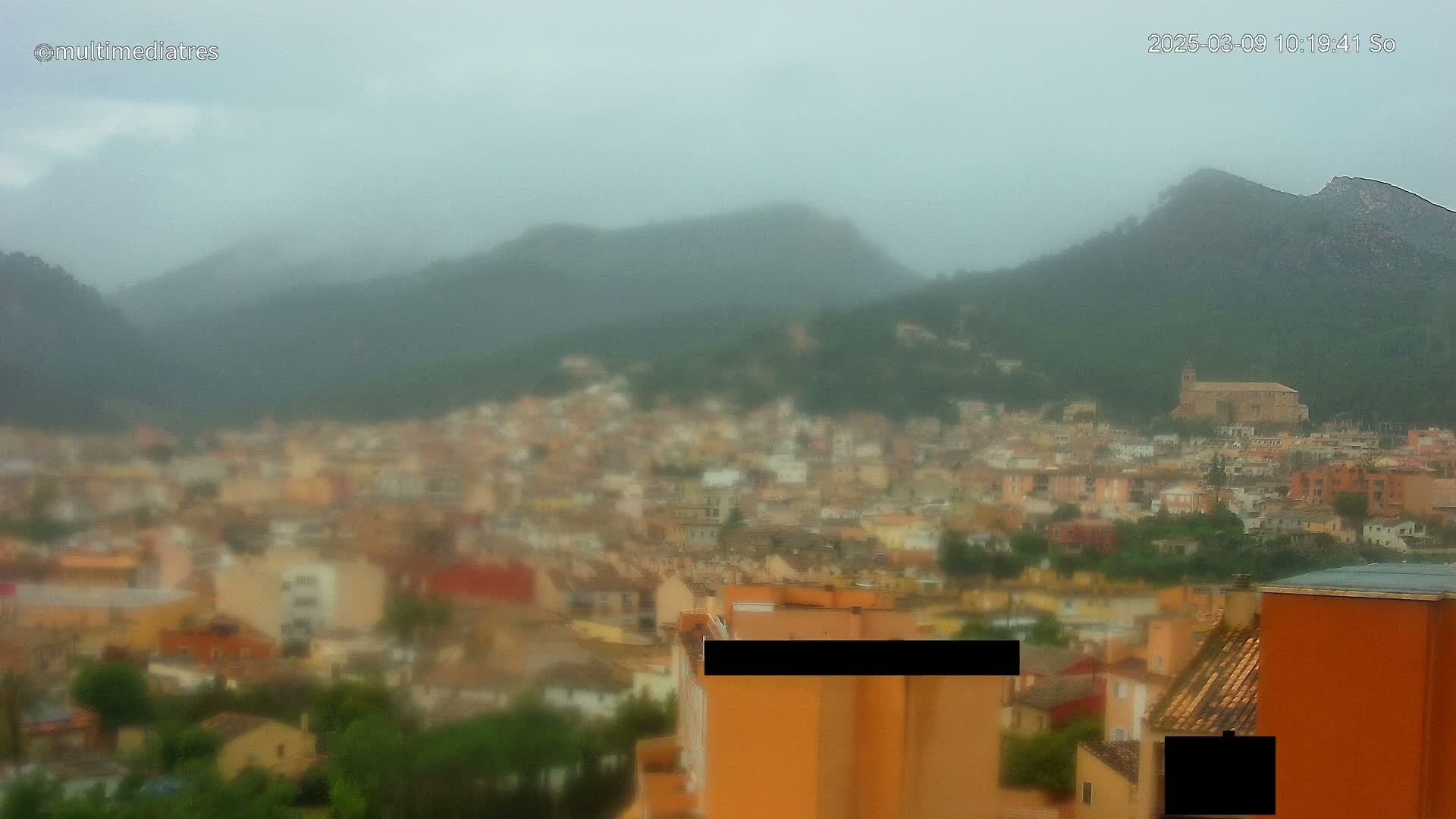 A rain-blurred view of a town nestled in a mountainous region.