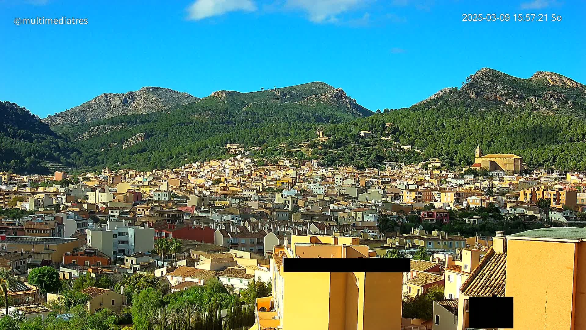 A sprawling town nestled in a valley between verdant, mountainous terrain under a clear blue sky.