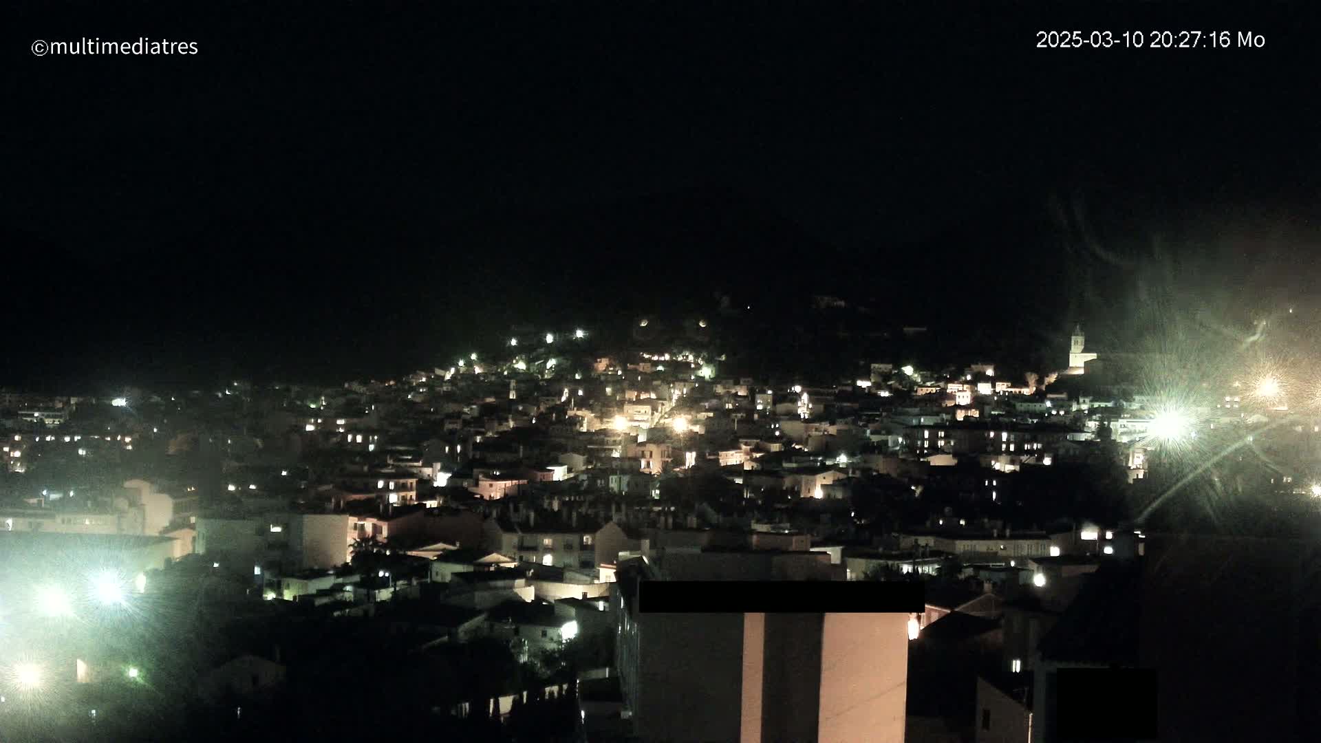 A nighttime view of a town nestled on a hill, illuminated by numerous lights.