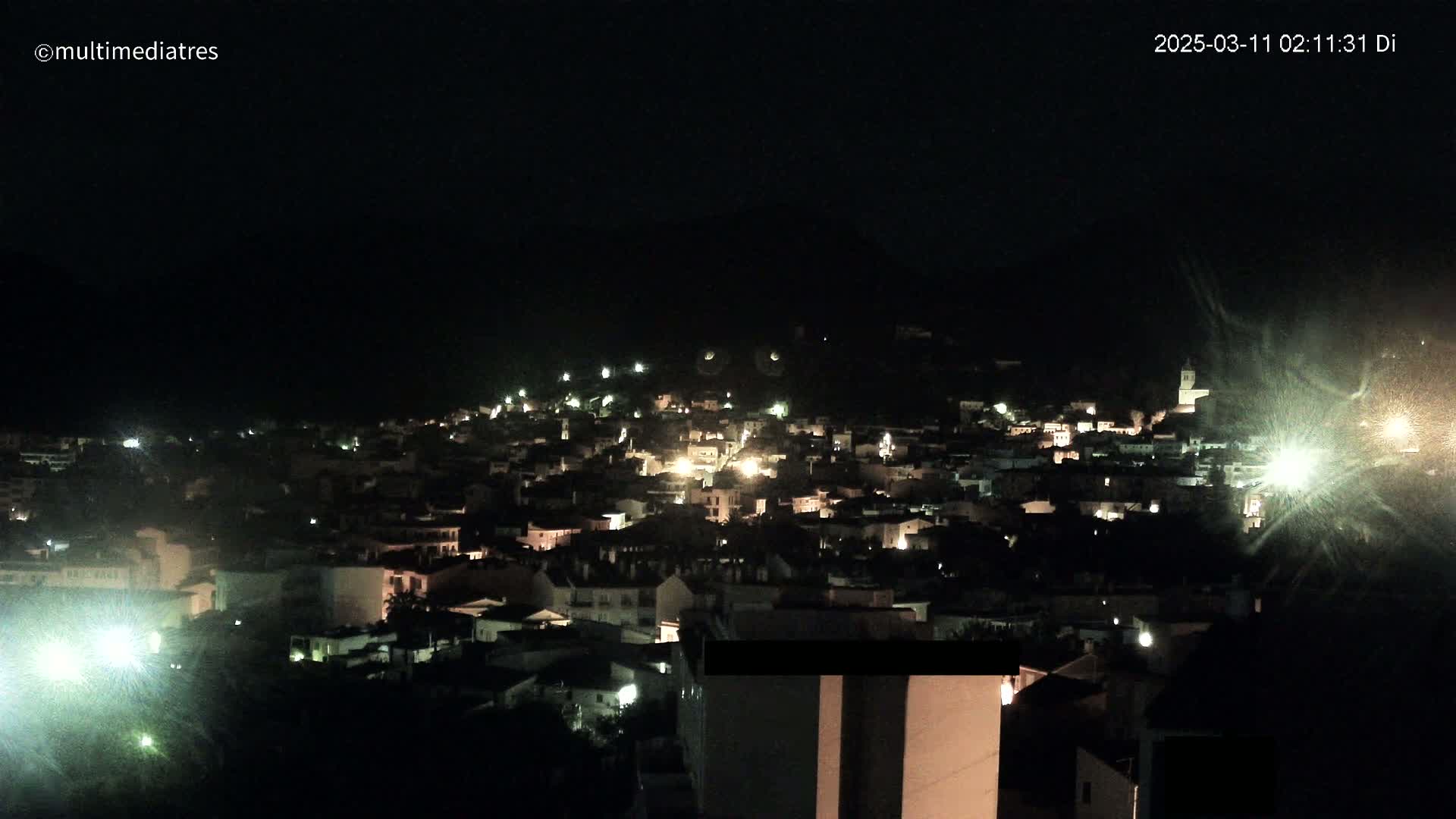 A nighttime view of a town nestled against a hill, illuminated by scattered lights.