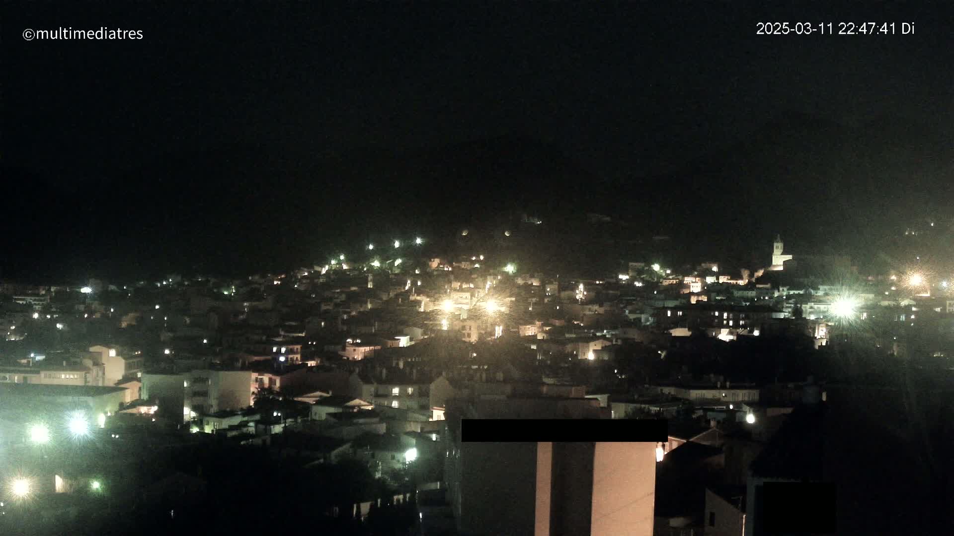 A nighttime view of a town illuminated by many lights on a hill under a clear, dark sky.