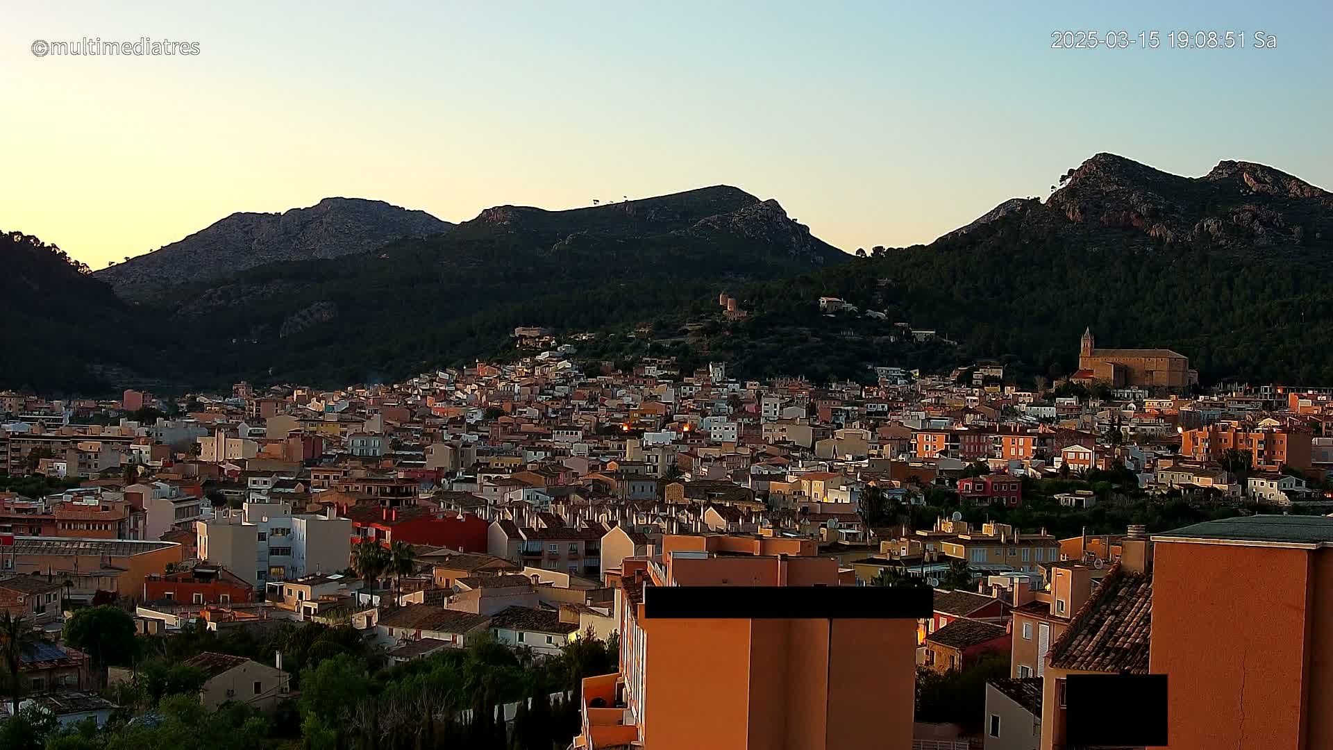 A sprawling town of low-rise buildings nestled against a mountain range at sunset under a clear sky.