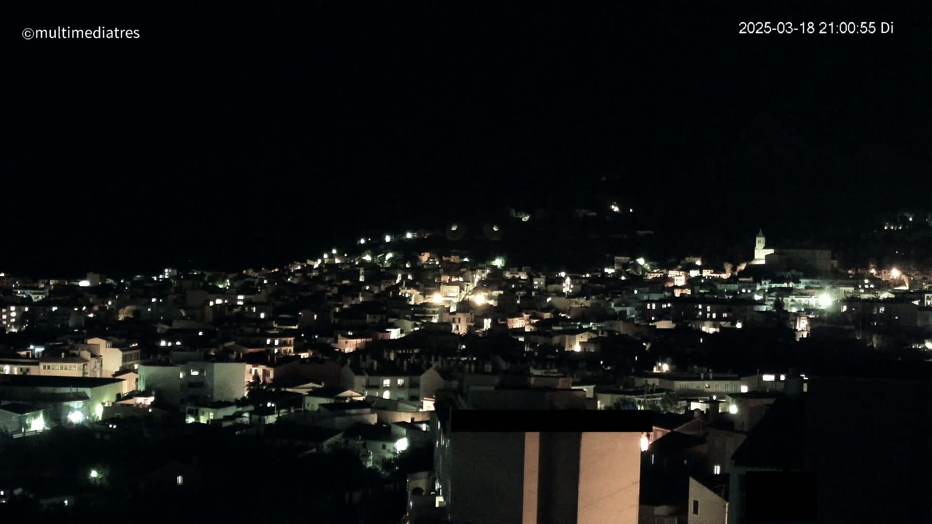 A nighttime view of a town nestled on a hillside, illuminated by scattered lights.