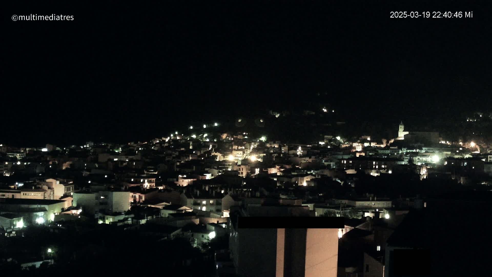 A nighttime view of a town nestled on a hill, illuminated by scattered lights.