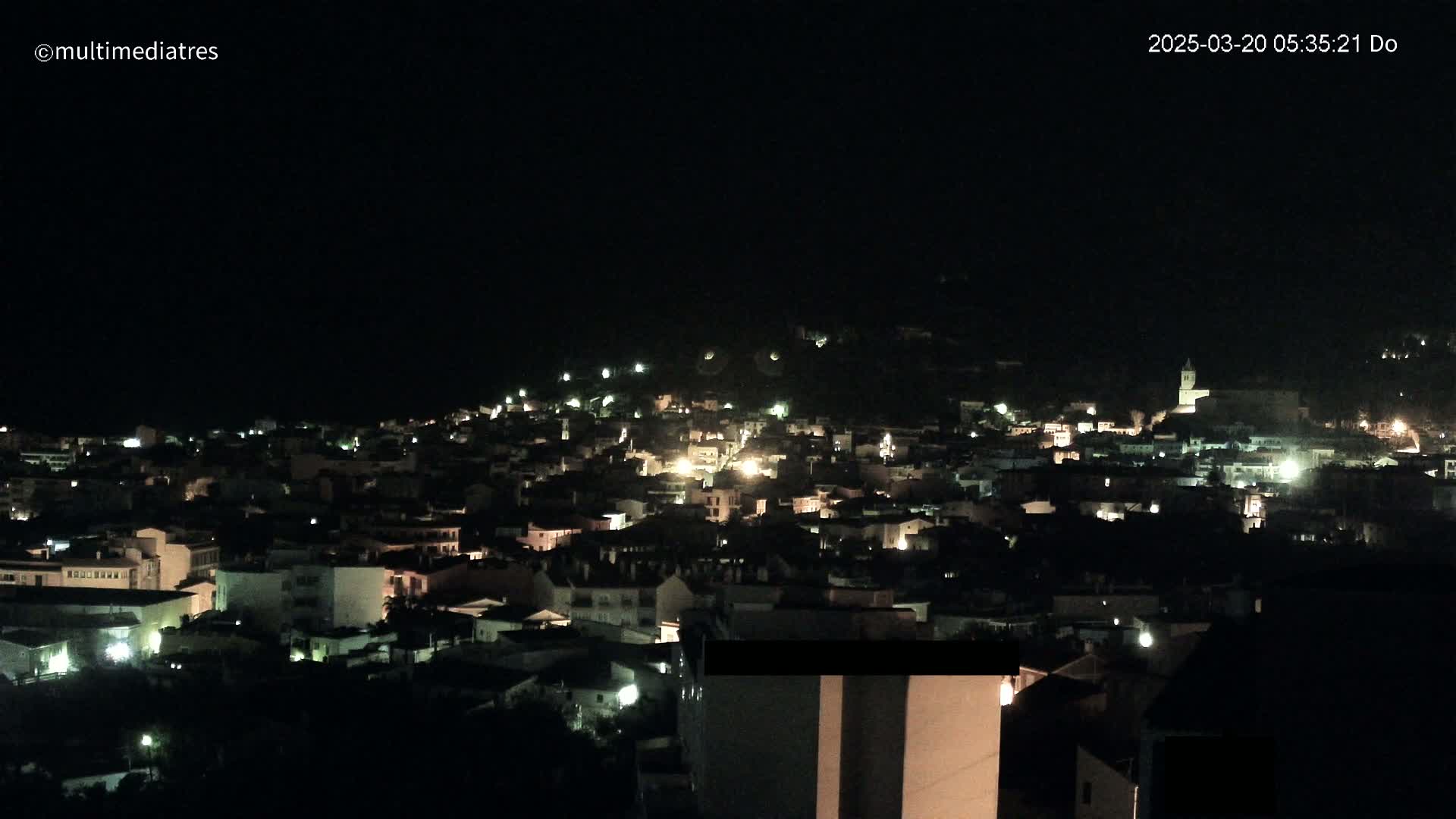 A nighttime, aerial view shows a small town illuminated by scattered lights on a hill.