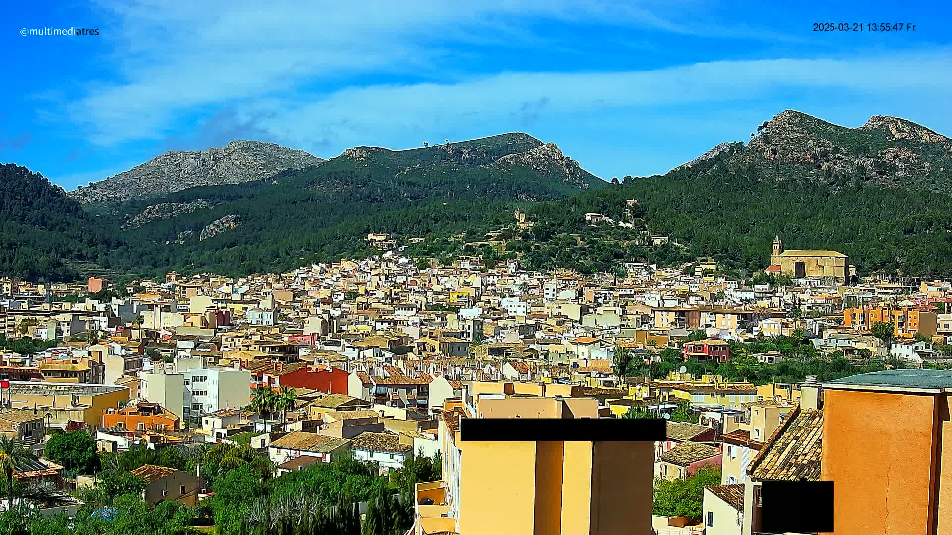 A sprawling town nestled in a valley between verdant, mountainous terrain under a bright, sunny sky.