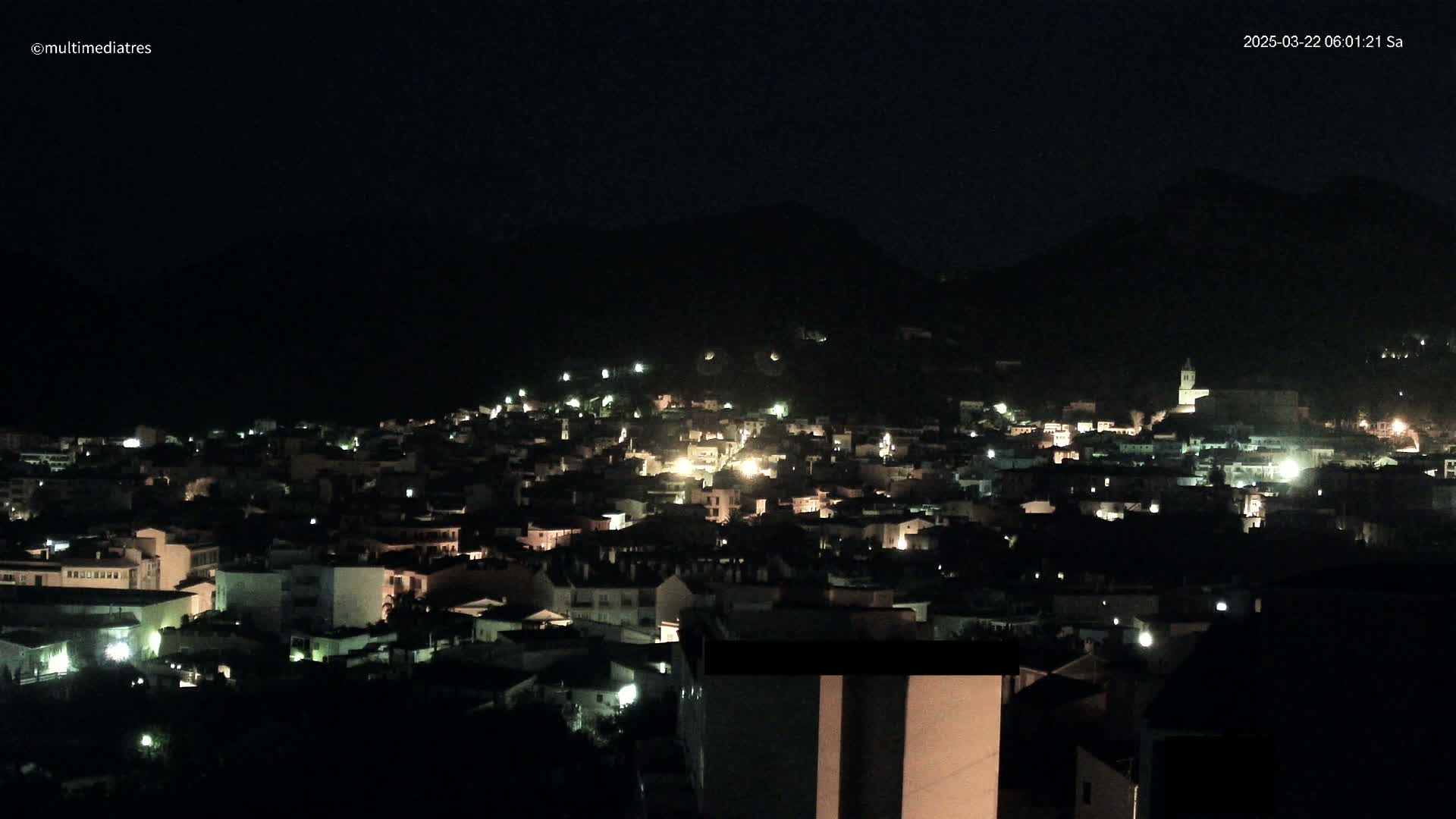 A nighttime view of a town nestled in a dark hillside, illuminated by scattered lights.