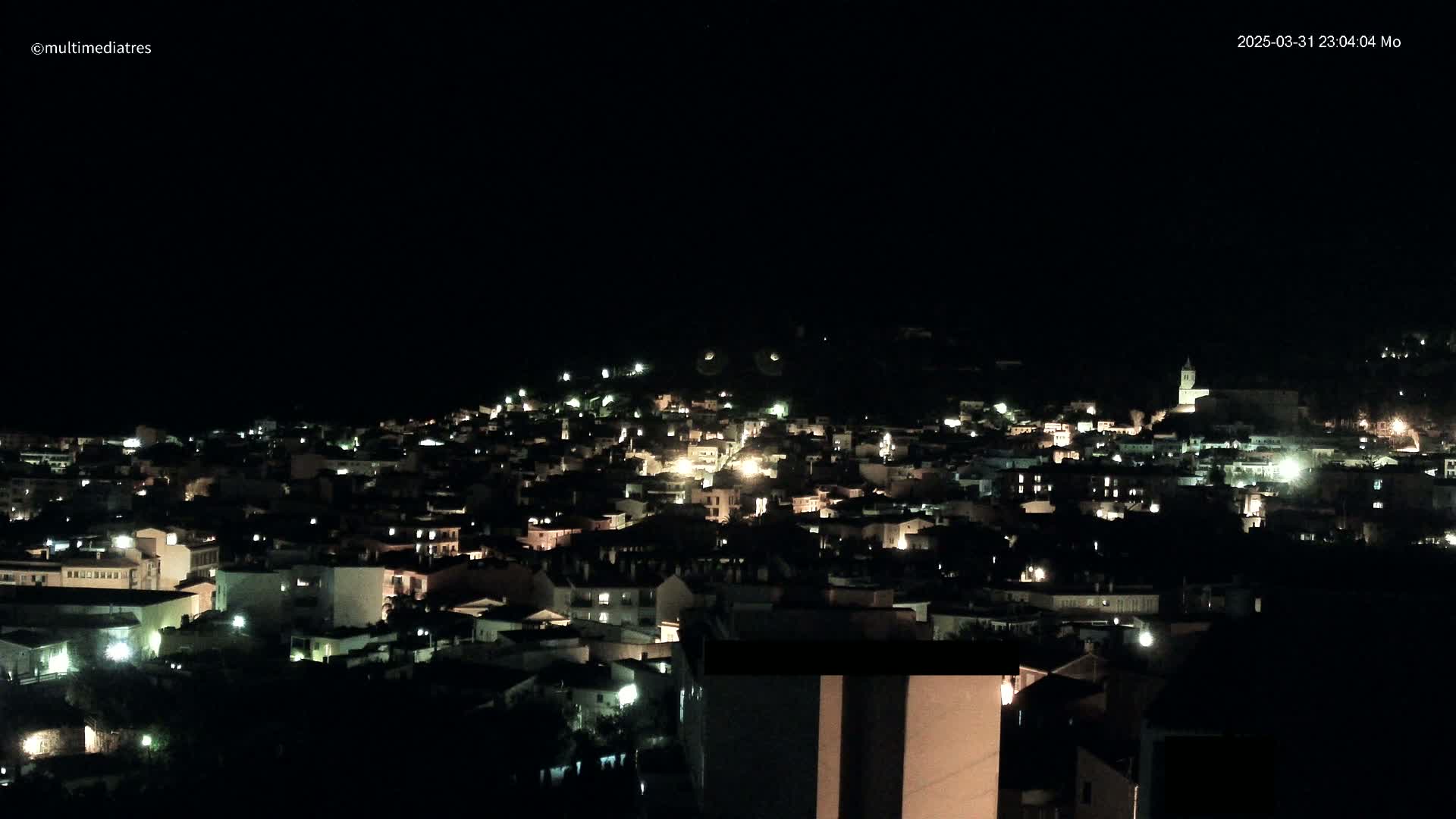 A hillside town is illuminated at night under a clear, dark sky.