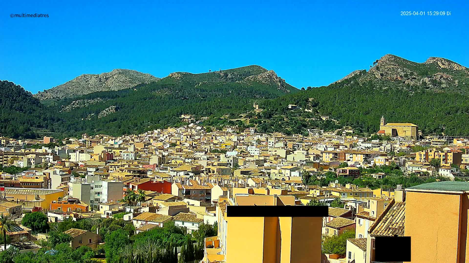 A sprawling town of low-rise buildings nestles at the foot of a mountain range under a clear blue sky.