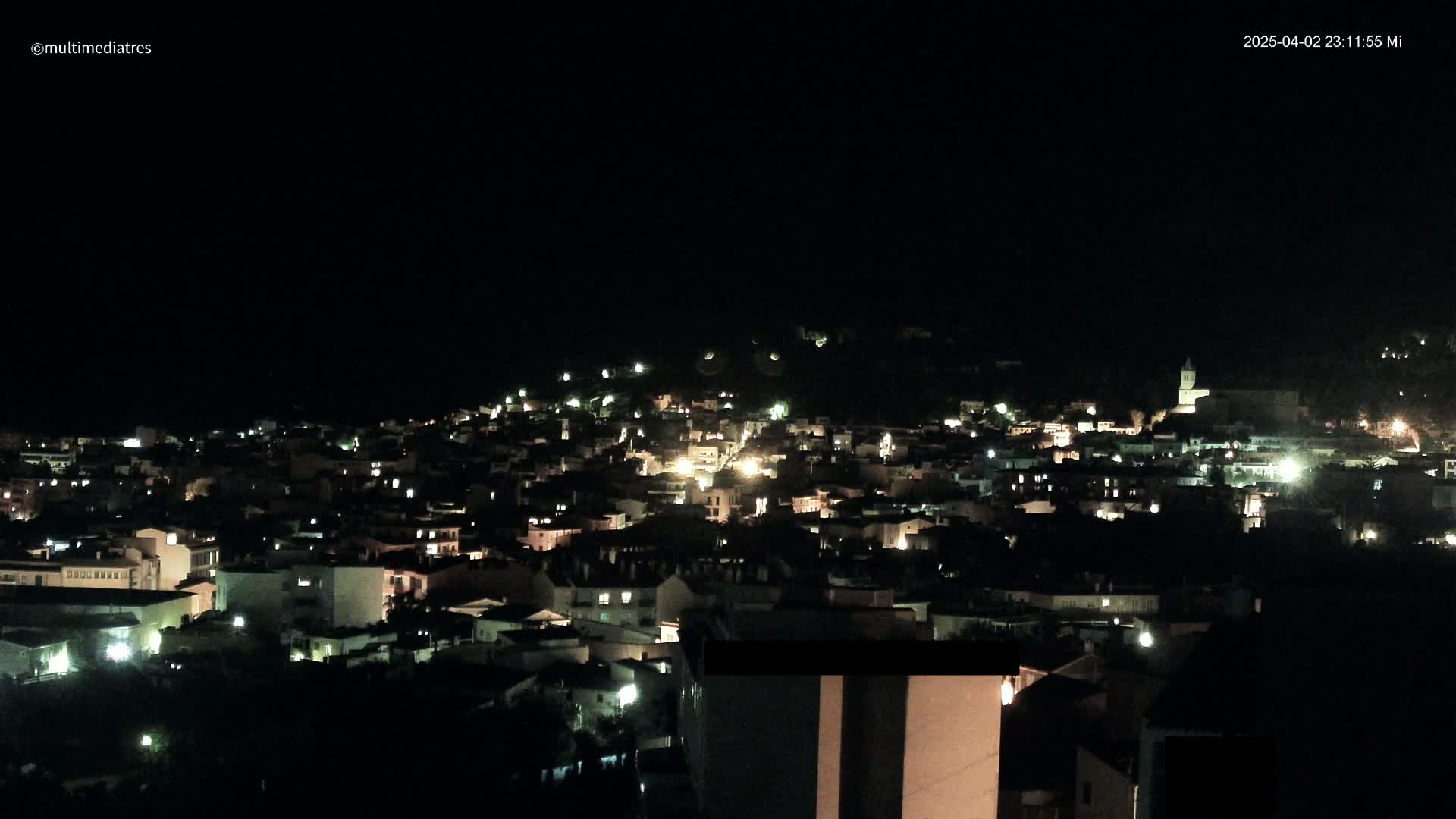 A nighttime view of a small town nestled on a hillside, illuminated by scattered lights.