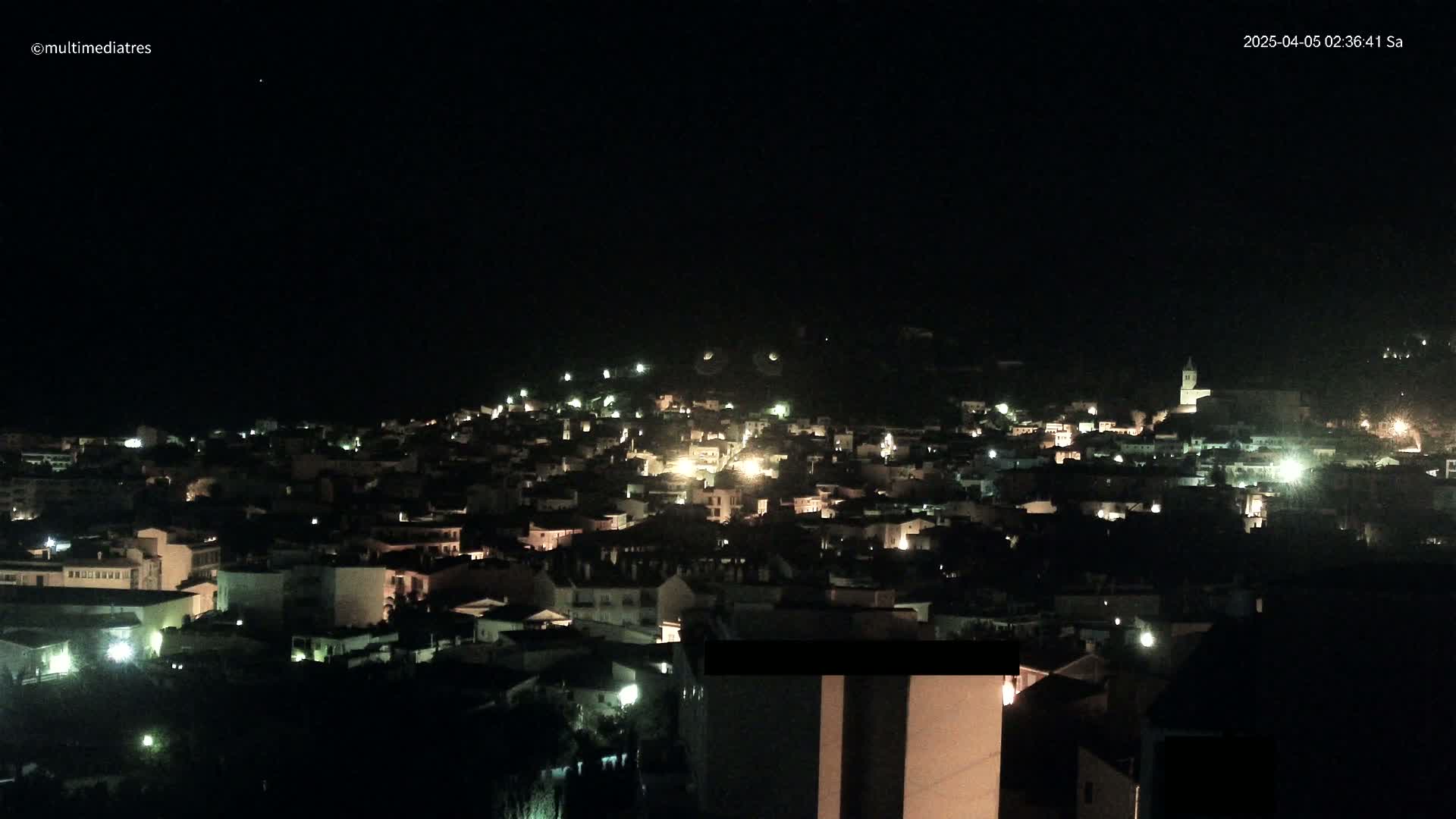 A nighttime view of a town illuminated by scattered lights under a clear, dark sky.