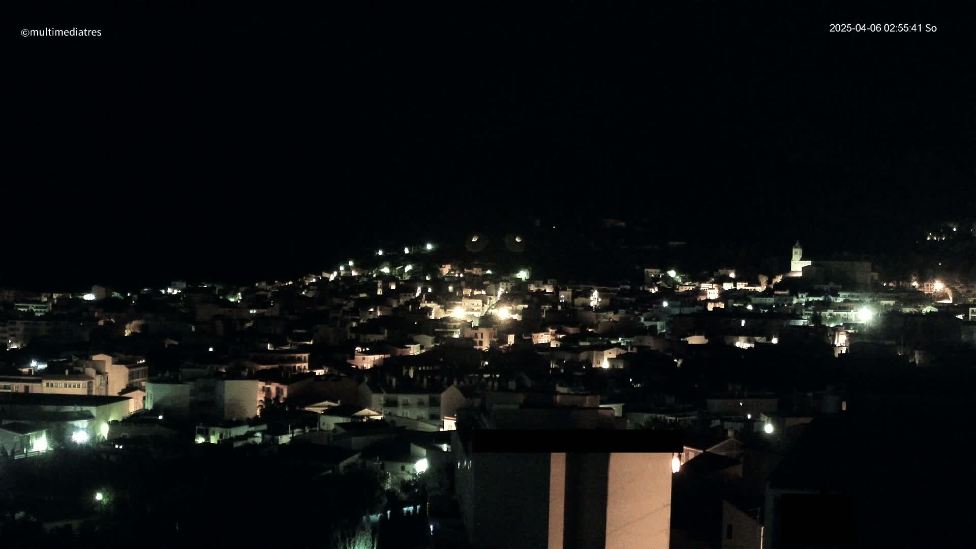 A nighttime view of a small town nestled on a hillside, illuminated by scattered lights.