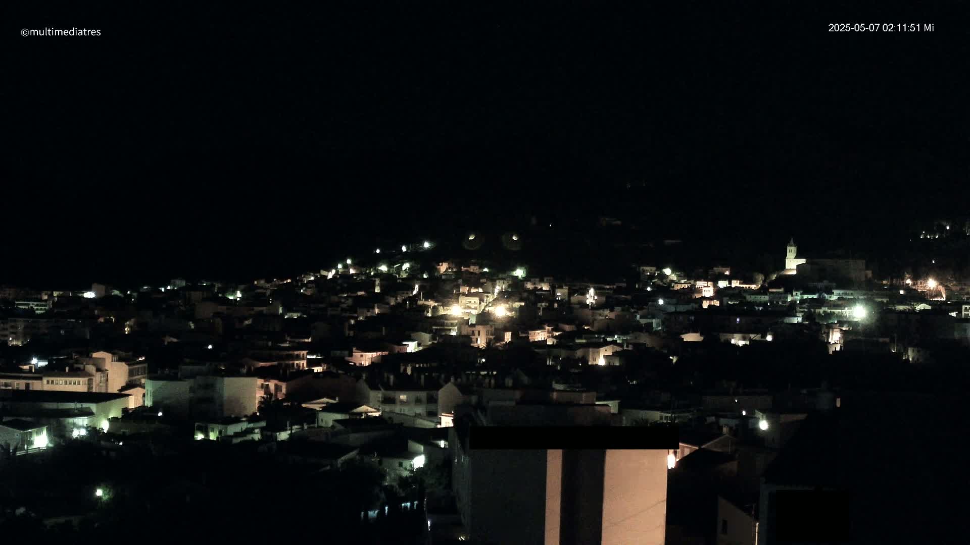 A nighttime, aerial view of a town illuminated by scattered lights under a dark sky.