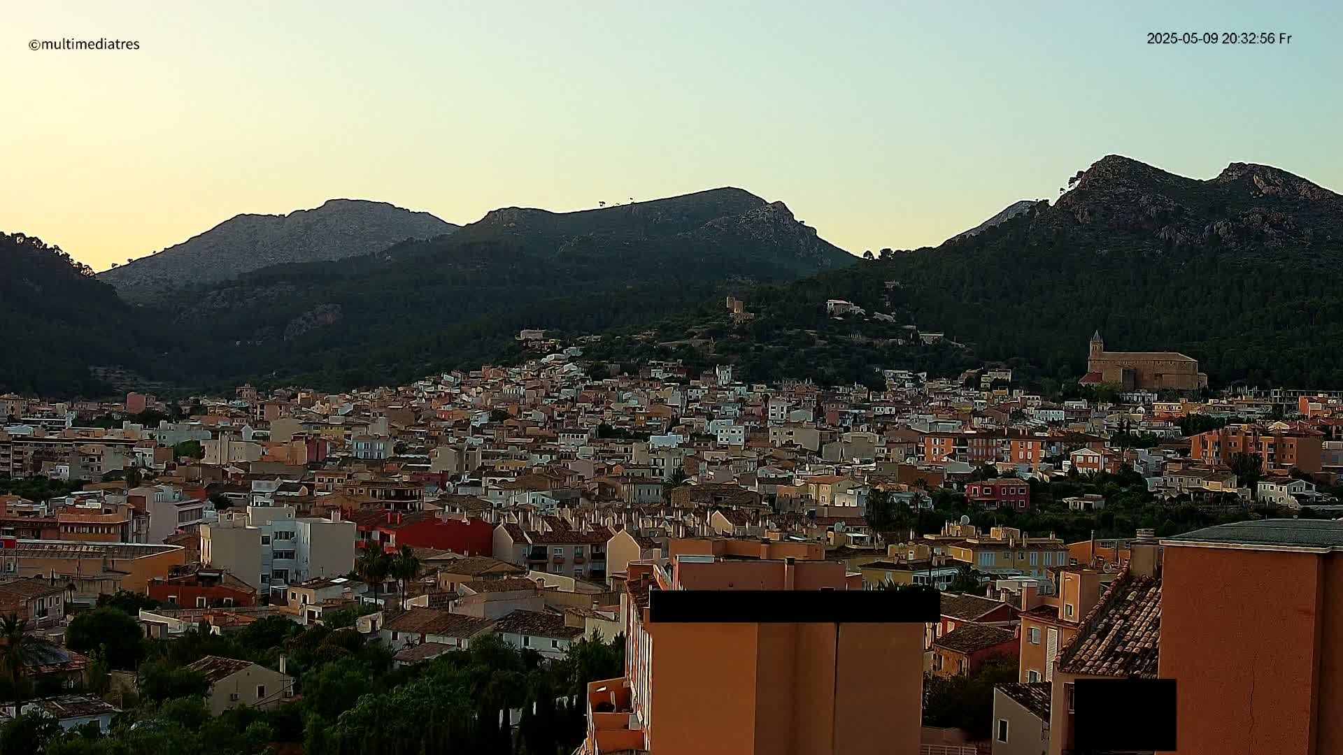 A dense collection of buildings nestled at the base of a mountain range under a twilight sky.