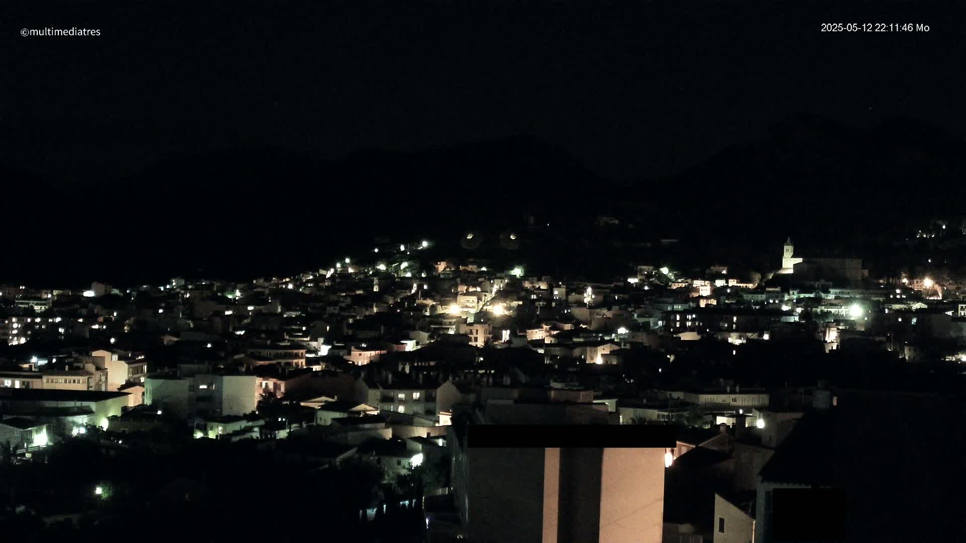 A nighttime view of a town nestled in a dark, hilly landscape under a clear, starlit sky.