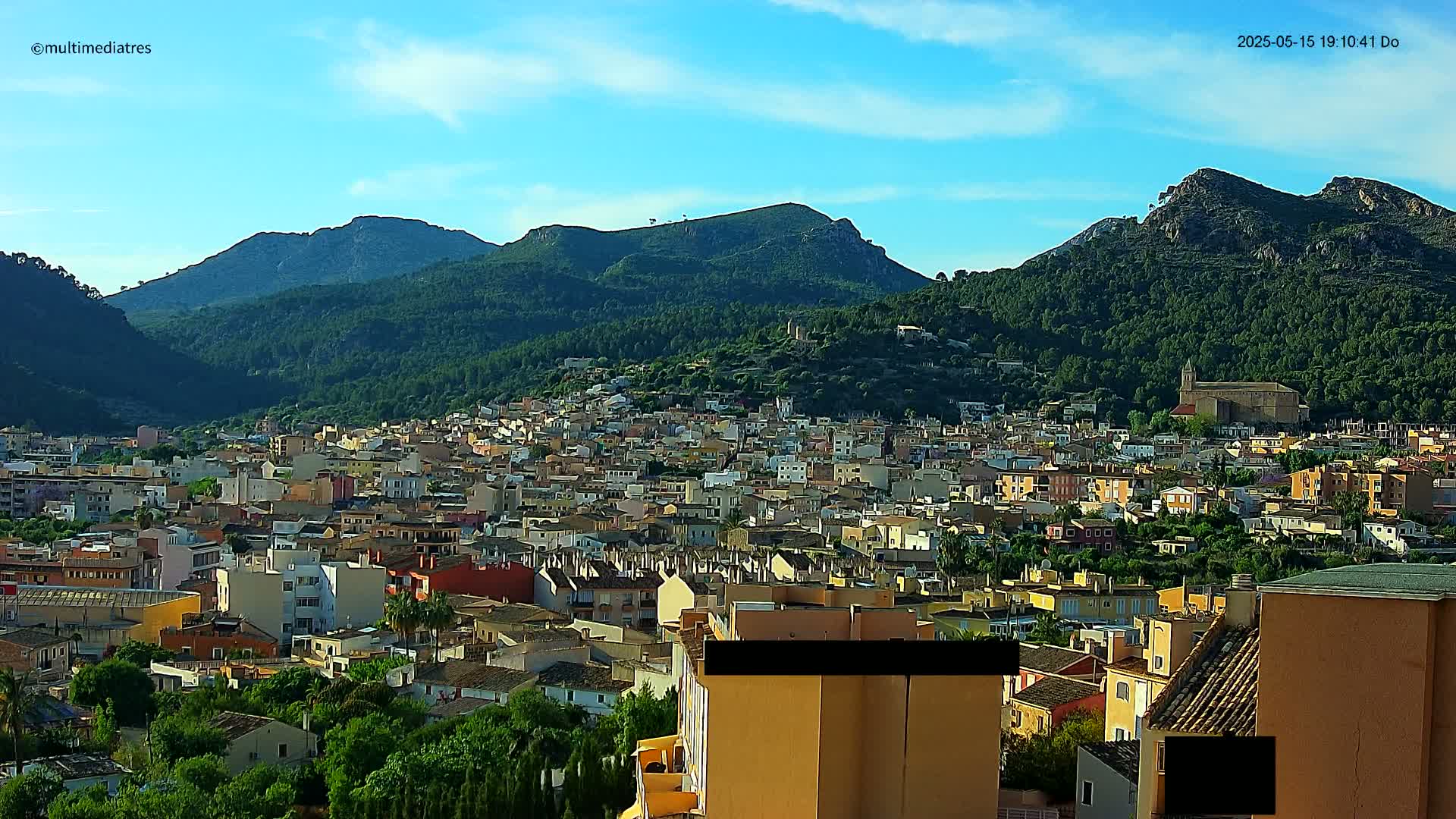 A sprawling town nestles in a valley surrounded by verdant, mountainous terrain under a clear, sunny sky.
