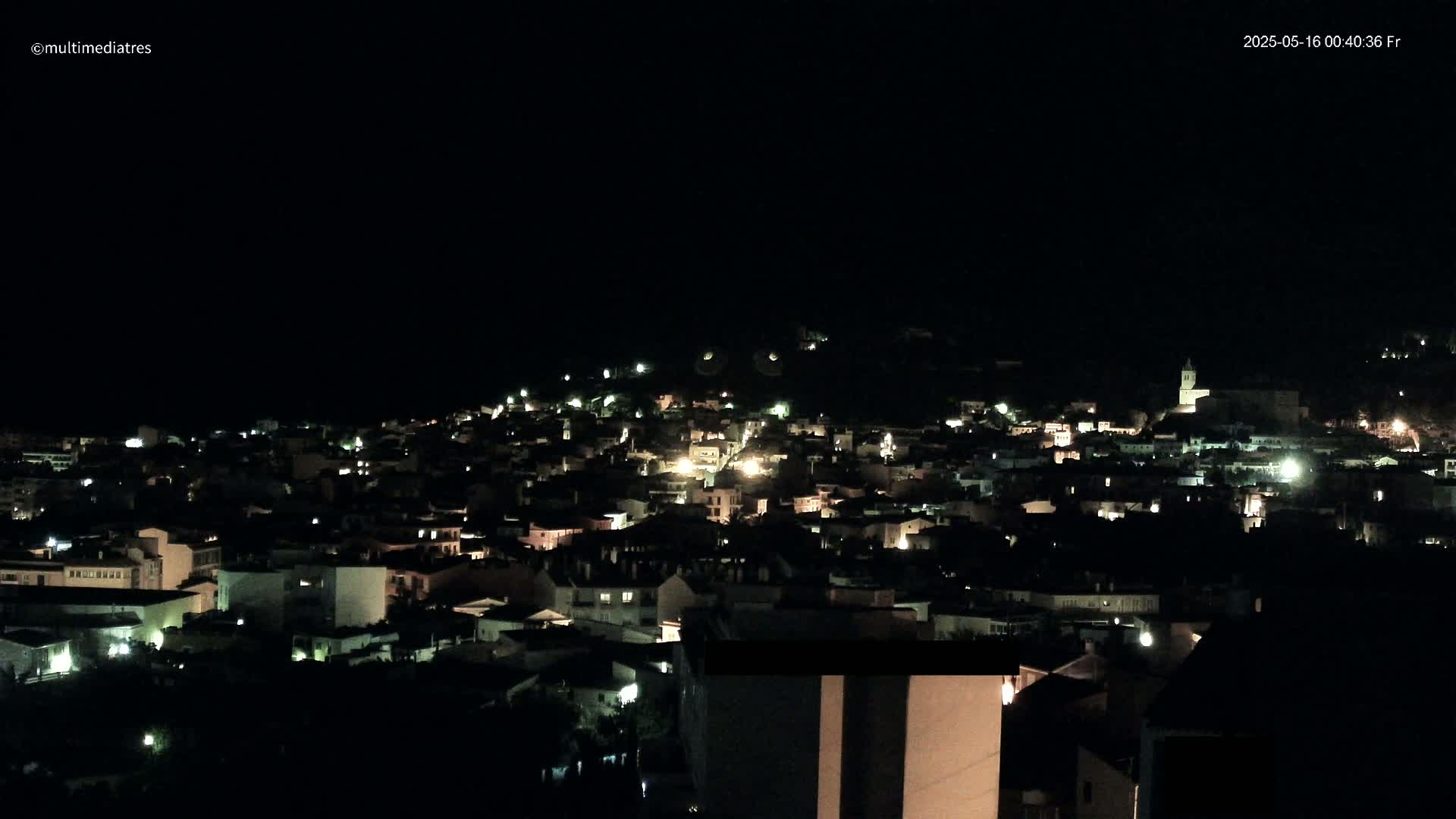 A nighttime view of a town nestled on a hill, illuminated by scattered lights.