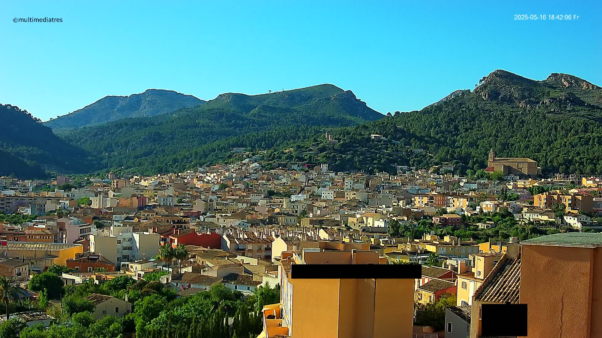 A sprawling town nestled in a valley, surrounded by lush green mountains under a clear blue sky.