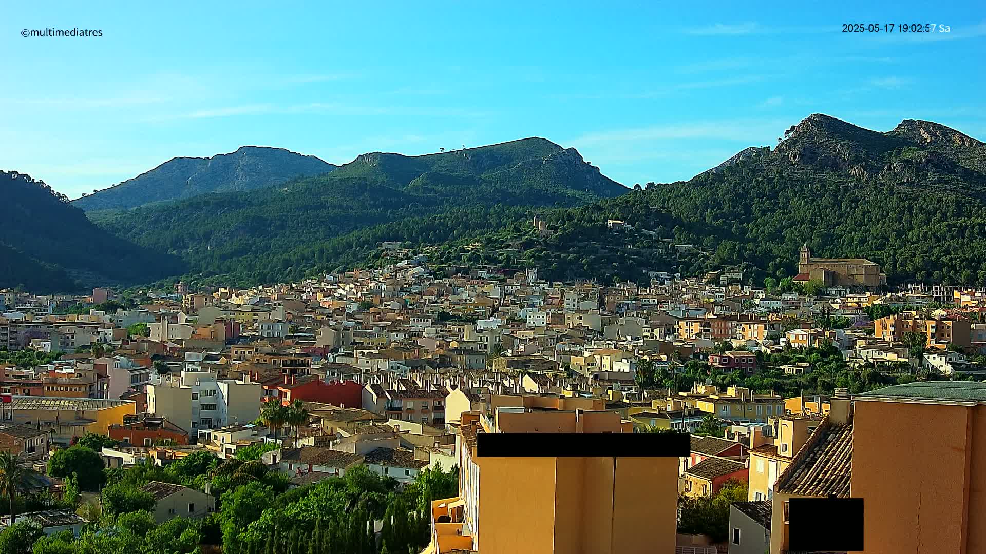 A sprawling town nestled in a valley between verdant, mountainous hills under a clear blue sky.
