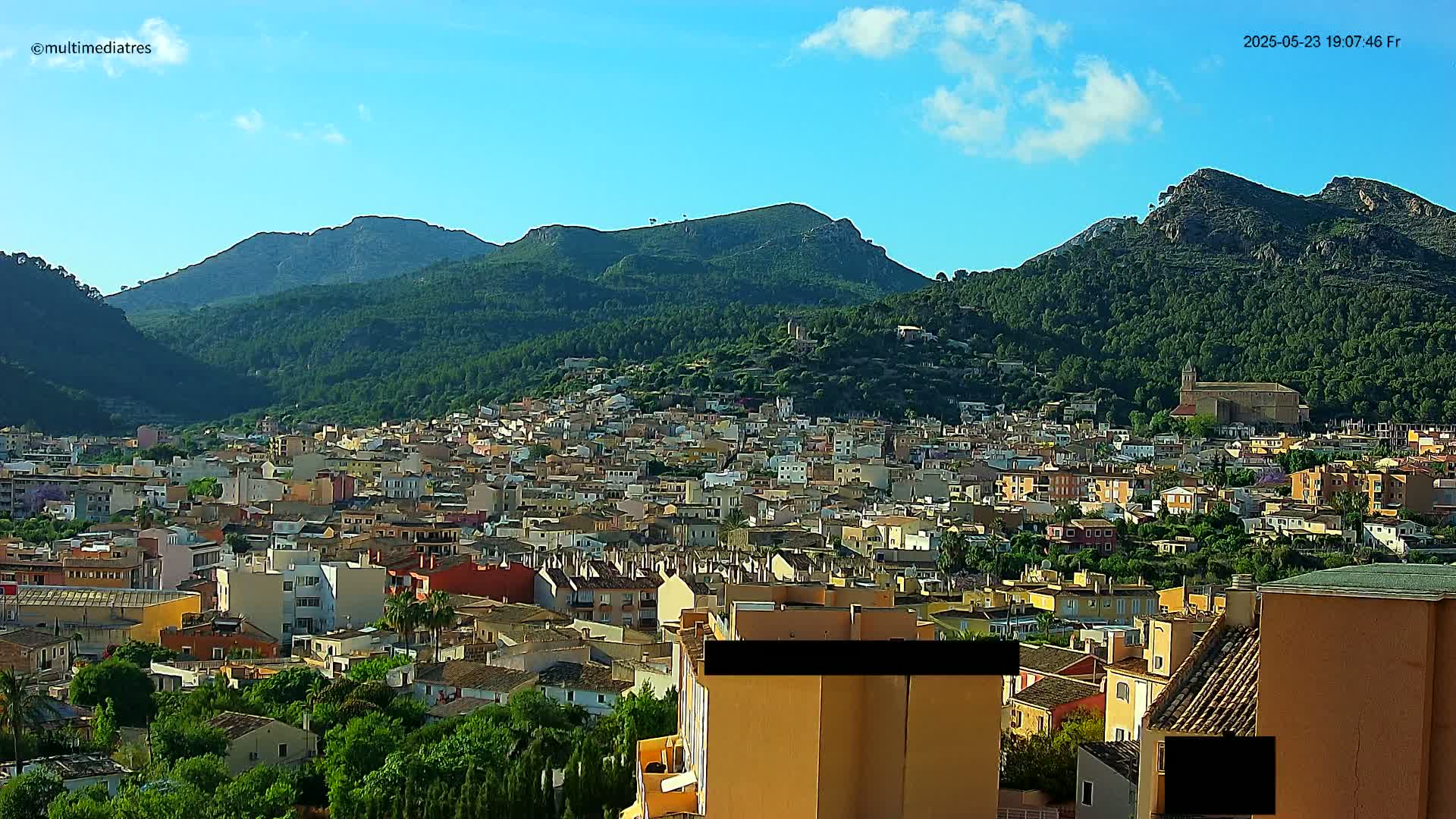 A sprawling town nestled in a valley, surrounded by lush green mountains under a clear blue sky.