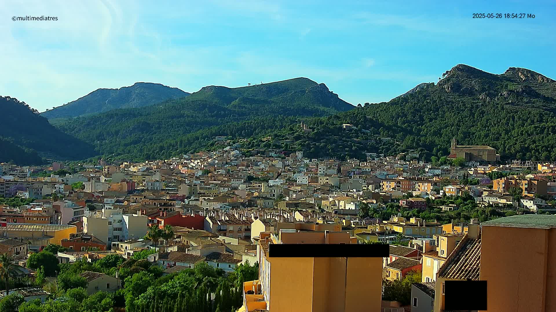 A sprawling town nestled in a valley, surrounded by lush green mountains under a clear blue sky.