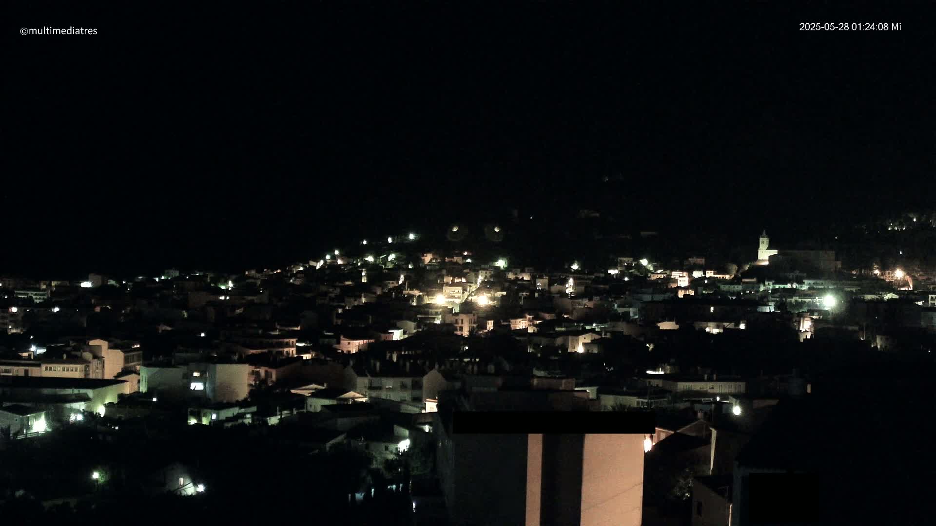 A nighttime view of a town illuminated by scattered lights under a dark, clear sky.