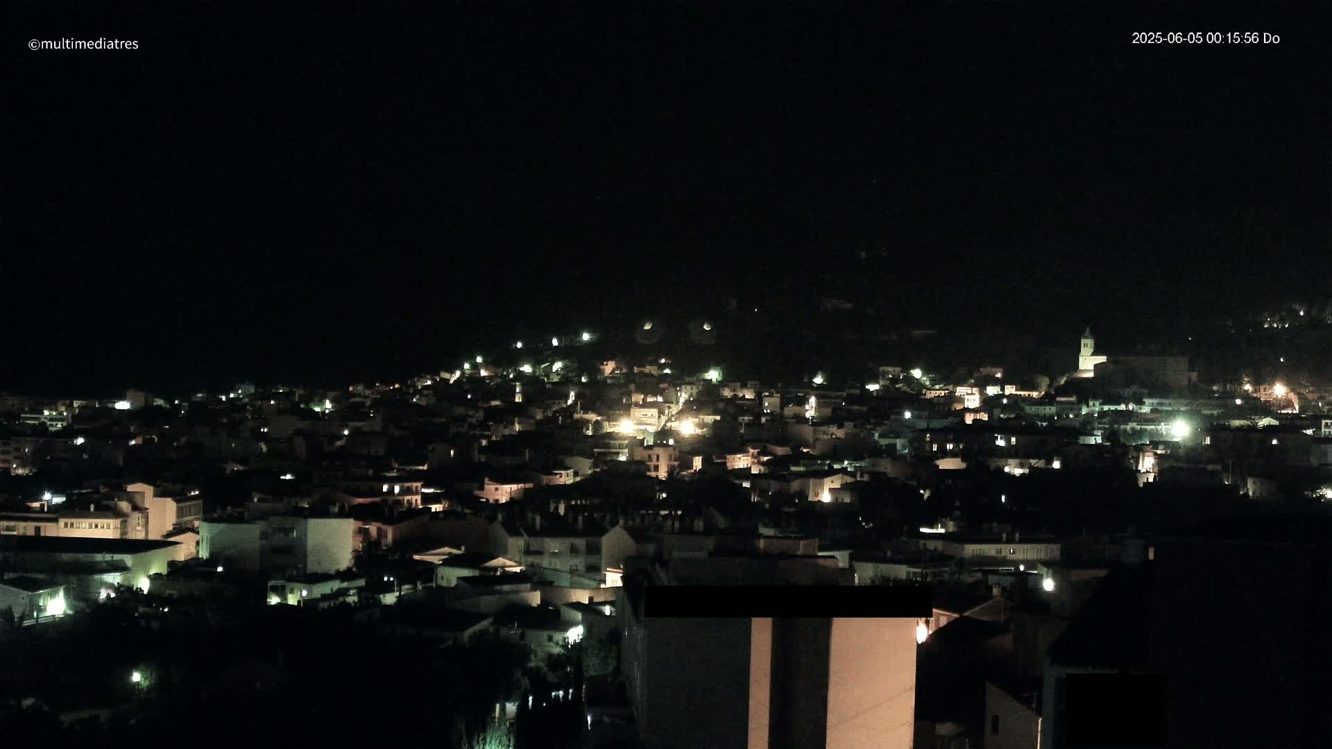 A nighttime, aerial view of a town with scattered lights illuminating buildings and streets under a dark sky.