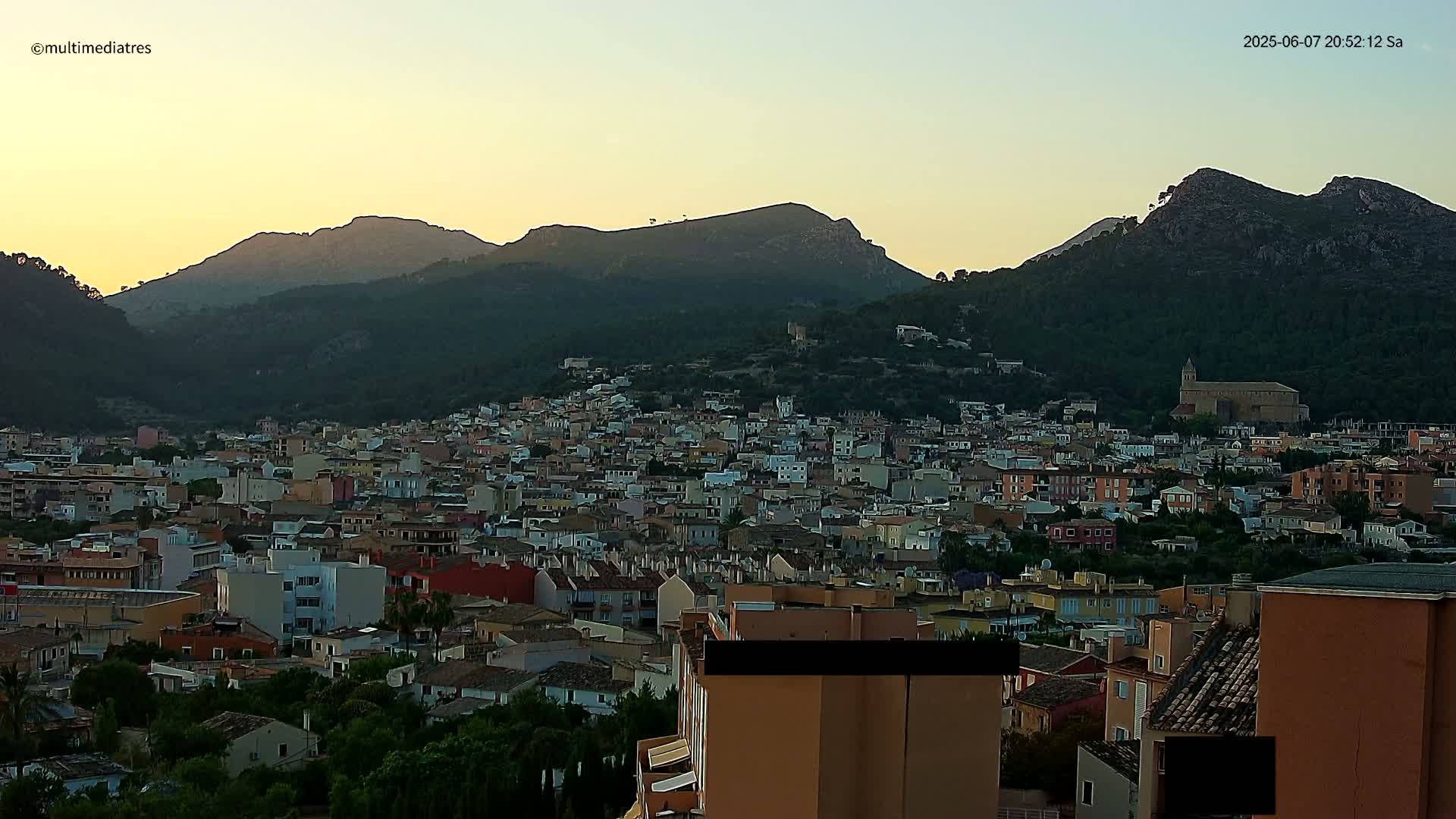 A sprawling town nestled in a valley between mountains, bathed in the soft light of sunset.