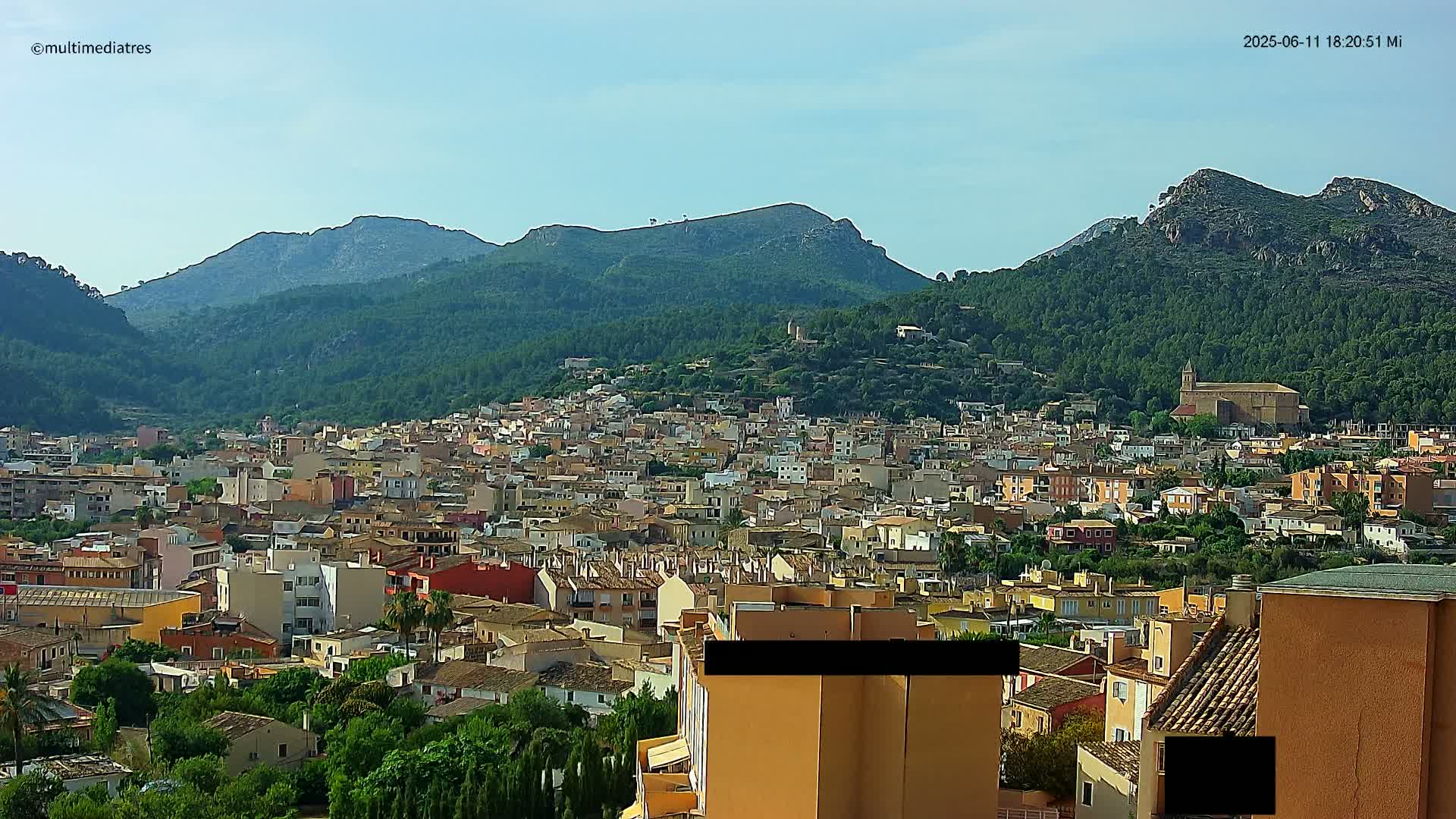 A sprawling town nestled in a valley, surrounded by lush green mountains under a clear, bright sky.