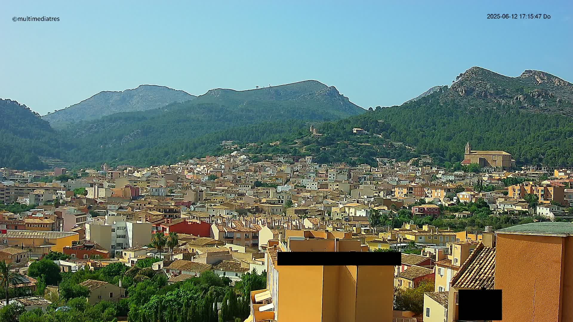 A sprawling town nestled in a valley between verdant mountains under a clear, sunny sky.