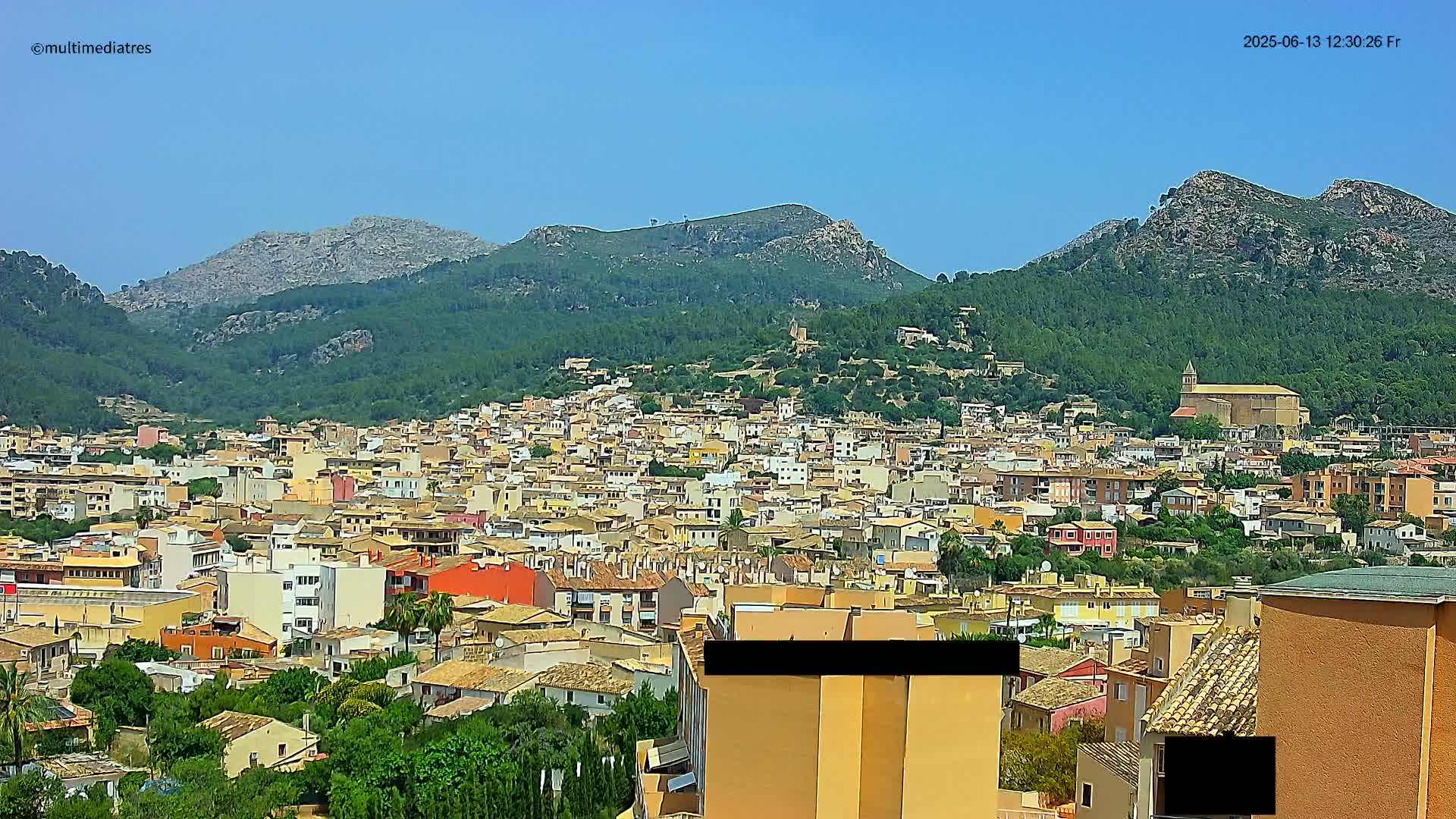 A sprawling town nestled in a valley, surrounded by lush green hills and mountains under a clear blue sky.