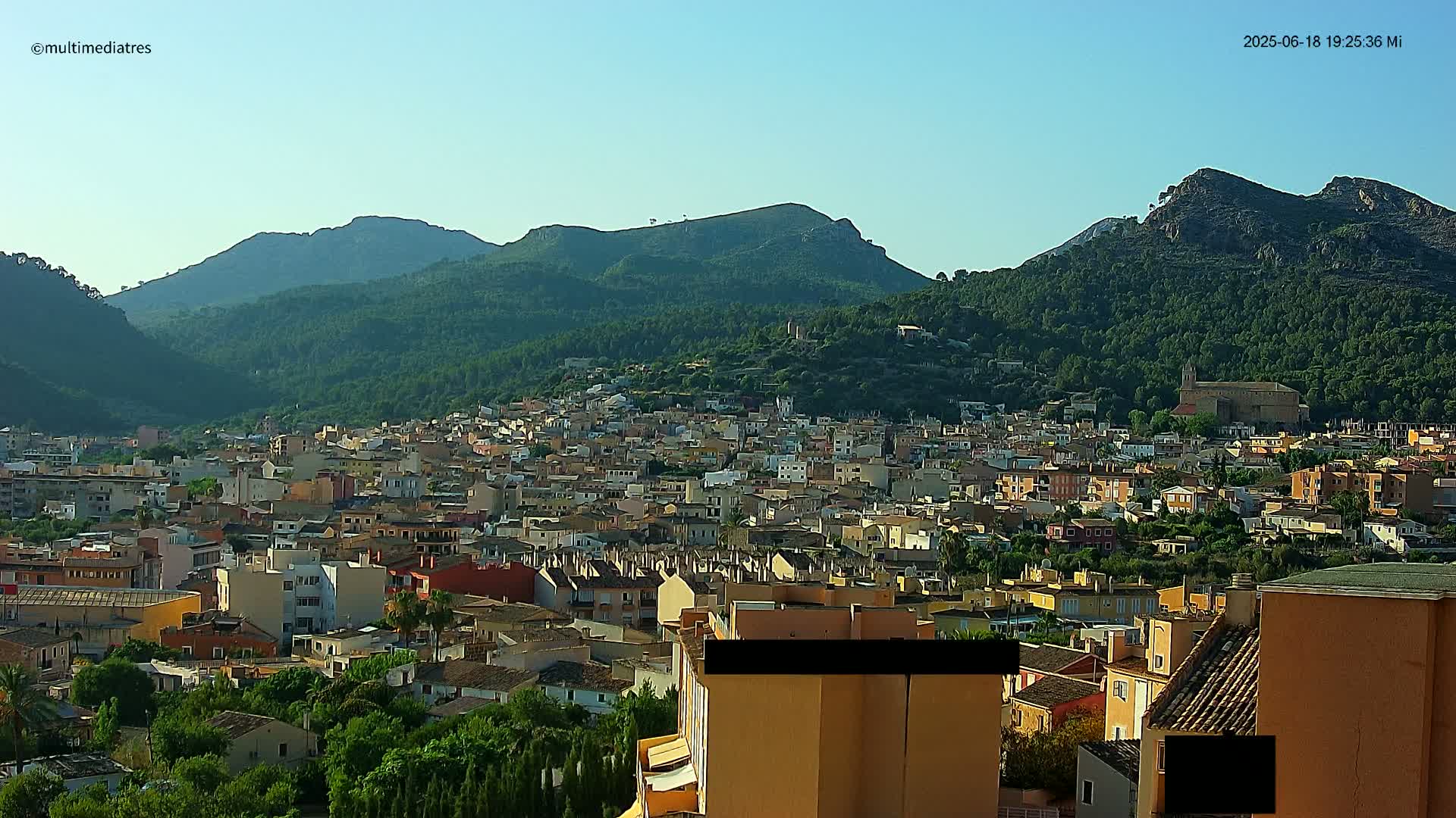 A sprawling town nestled in a valley, surrounded by lush green mountains under a clear, bright sky.