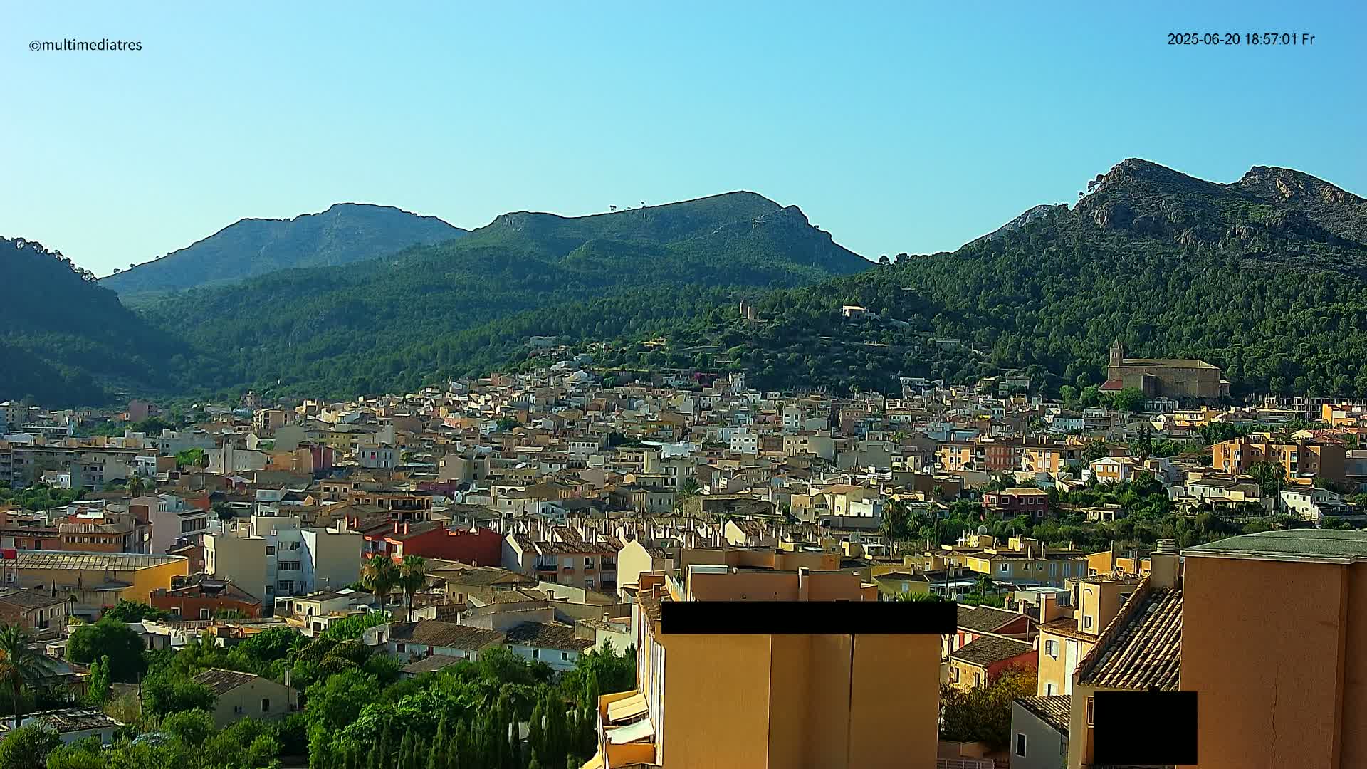 A sprawling town nestled at the base of verdant, mountainous terrain under a clear sky.