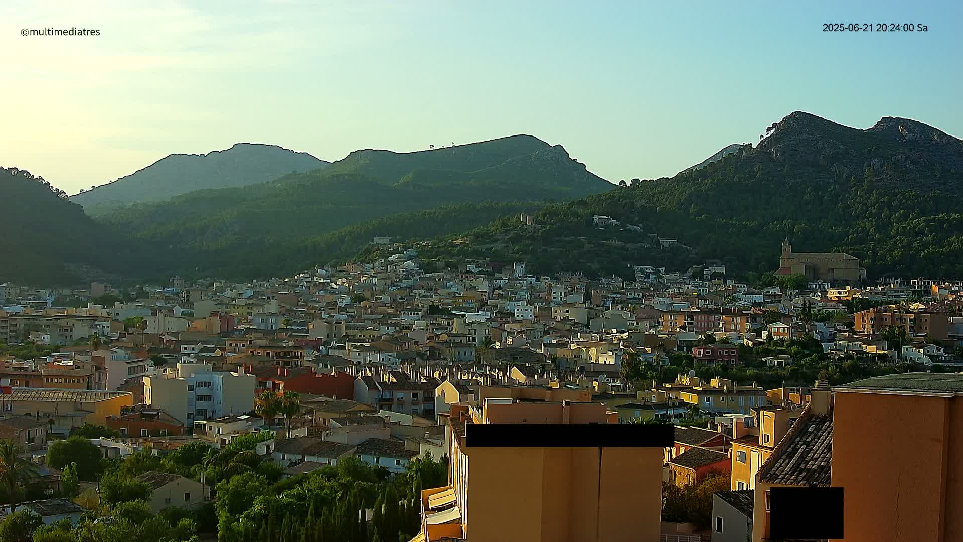 A town nestled in a valley, surrounded by lush green hills under a clear sky.