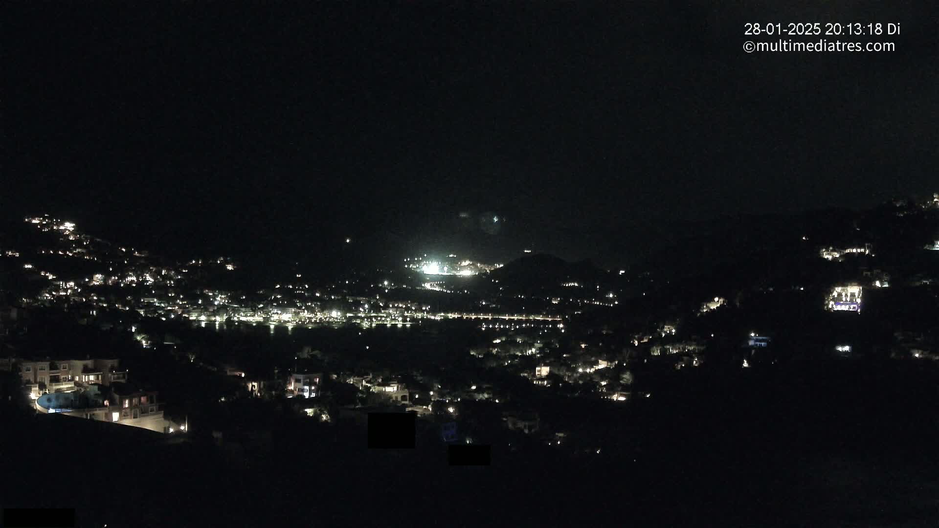 A nighttime view of a hillside town illuminated by scattered lights under a clear, dark sky.