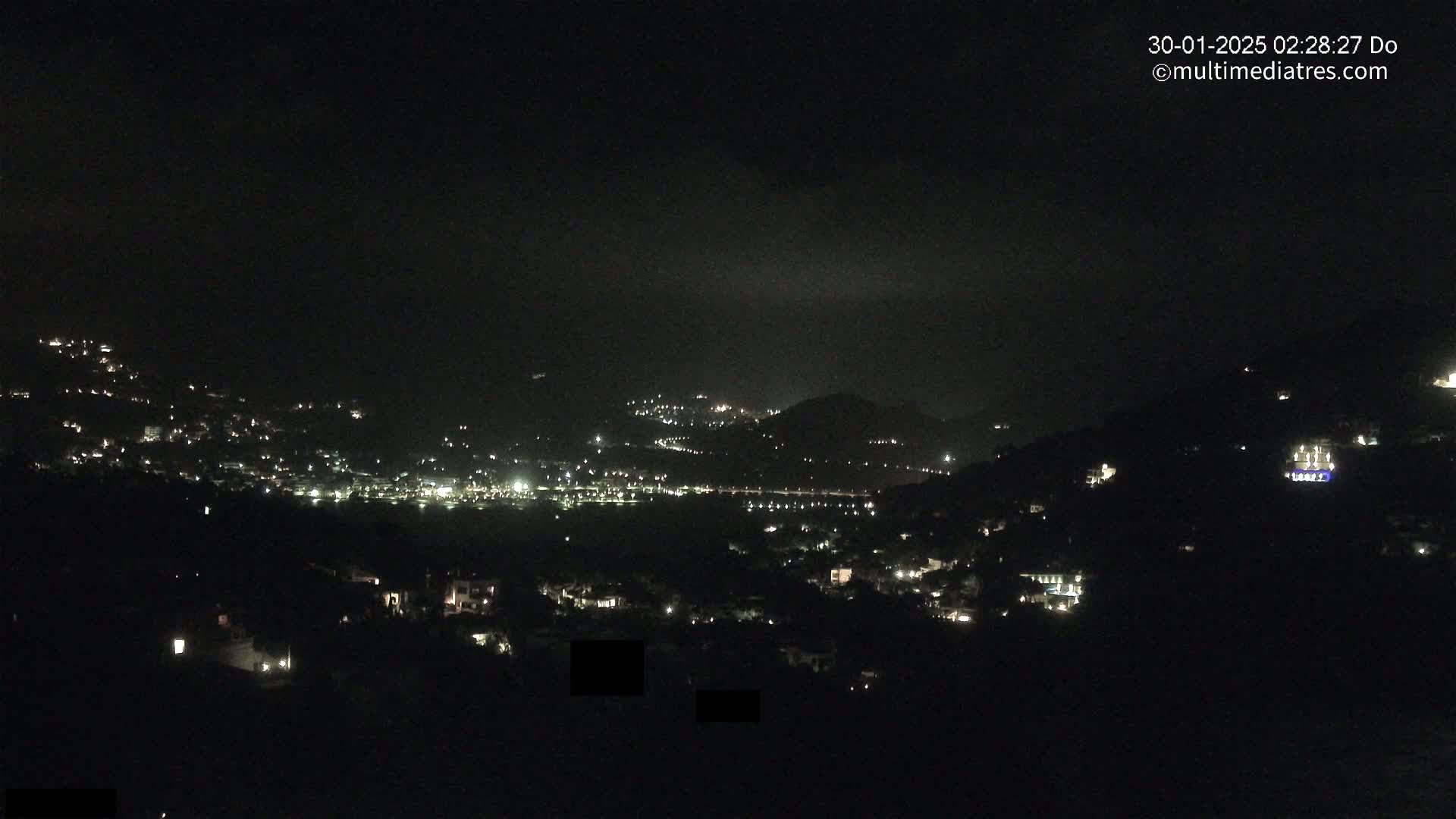 A nighttime view of a hillside town speckled with lights under a mostly clear, dark sky.