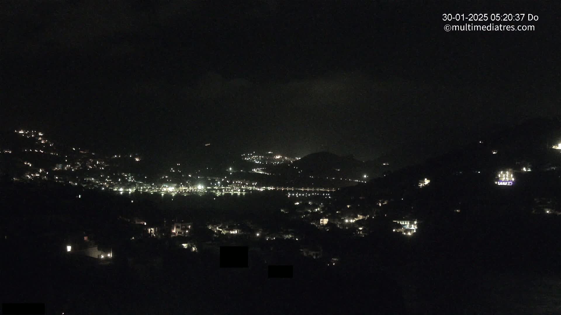 A nighttime view of a town nestled in hills, with scattered lights visible in the darkness.
