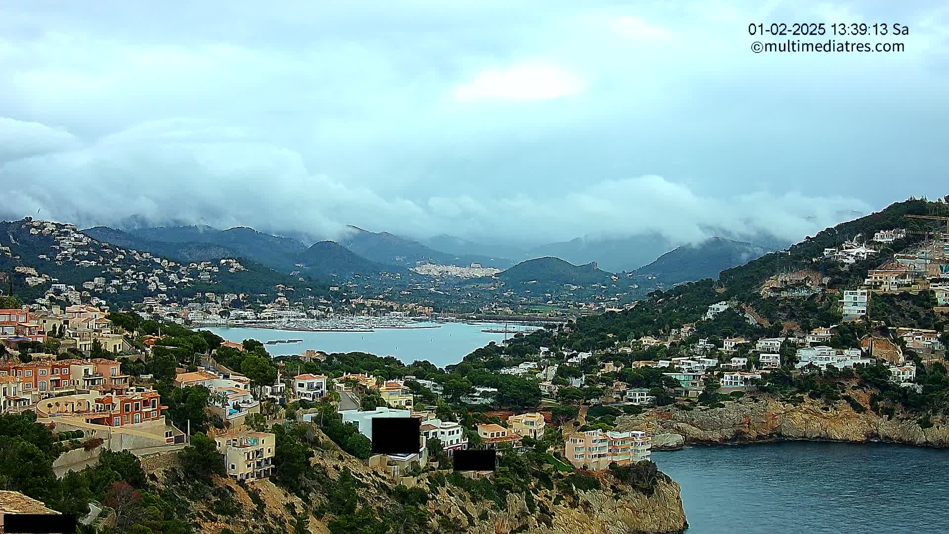 A coastal town with many houses built into a hillside overlooking a calm bay under a cloudy sky.