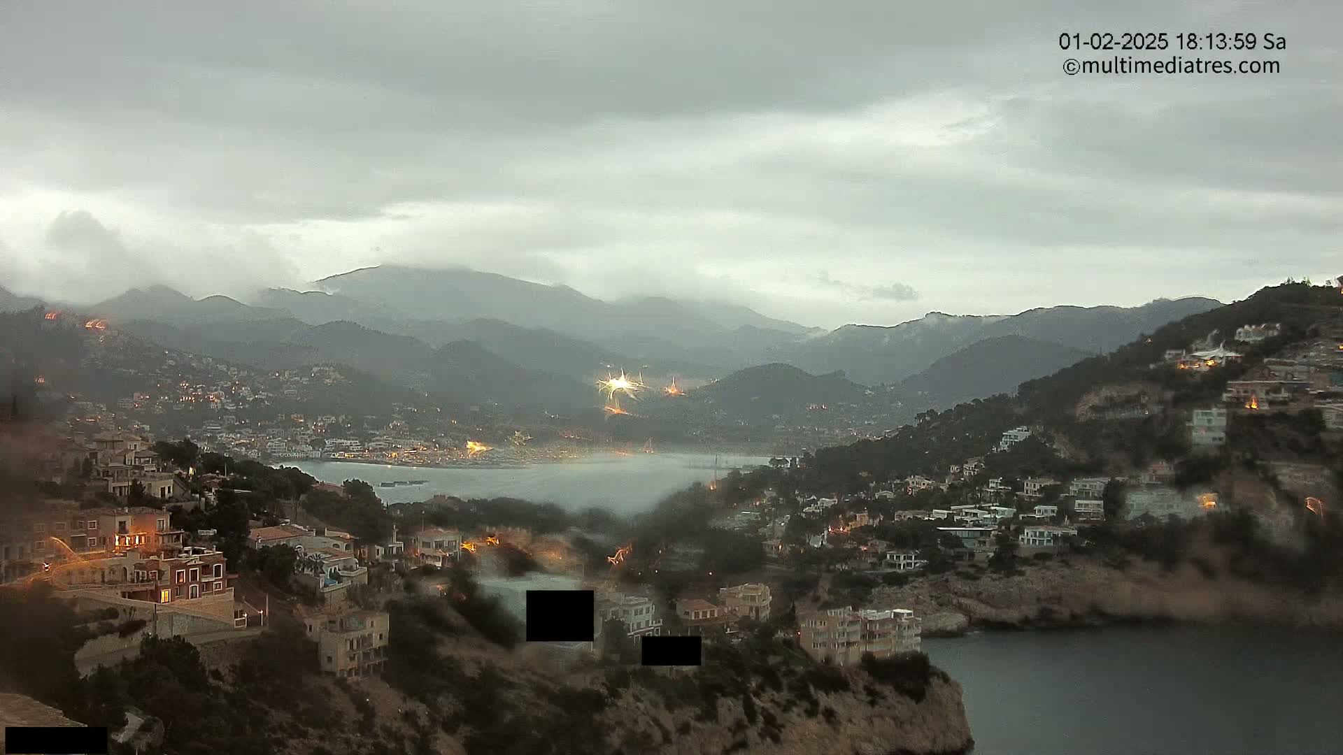 A coastal town nestled between hills and a calm bay under an overcast sky.