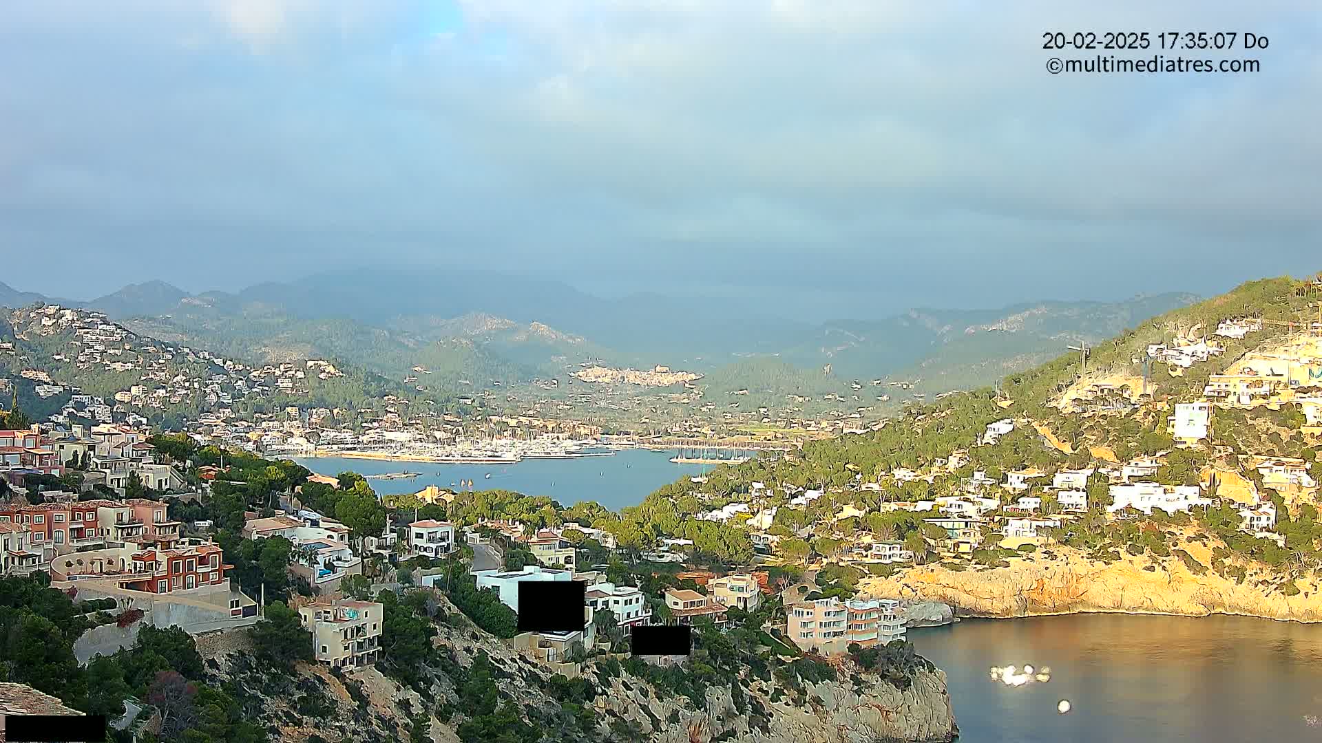 A coastal town nestled in hills overlooking a calm bay under a mostly clear sky.