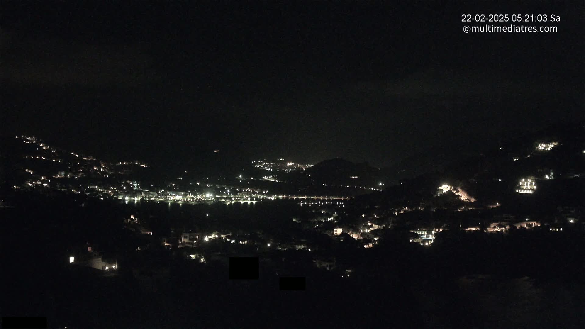 A nighttime view of a town nestled on hillsides, with scattered lights illuminating the landscape under a clear, dark sky.