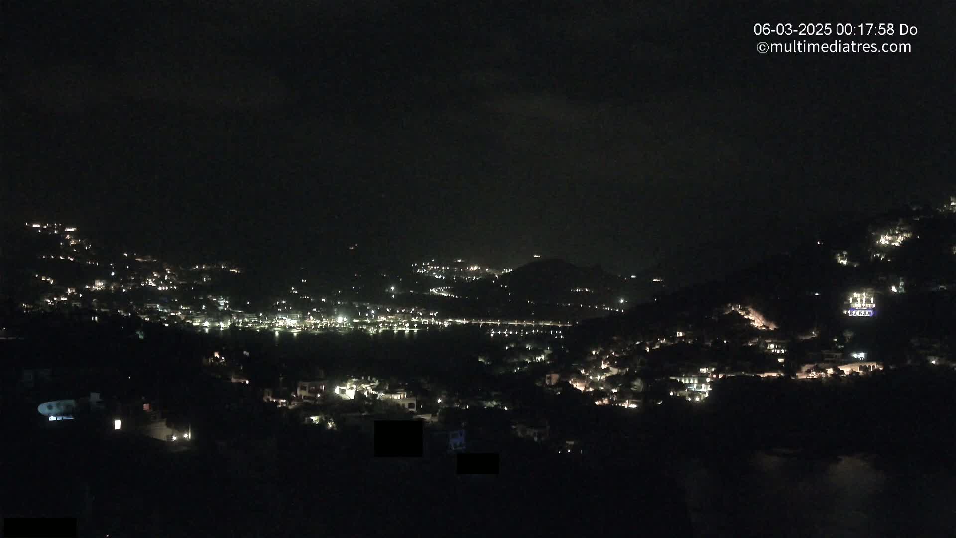 A nighttime view of a hillside town with scattered lights, under a dark, clear sky.