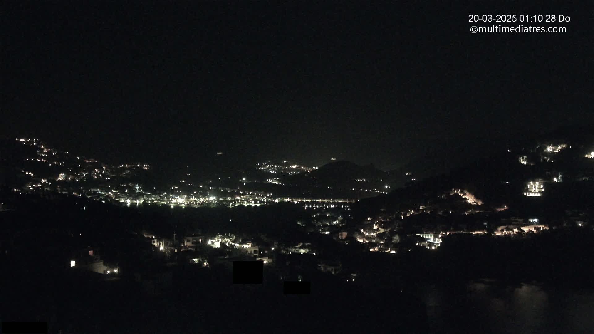 A nighttime view of a town nestled in hills, illuminated by scattered lights.