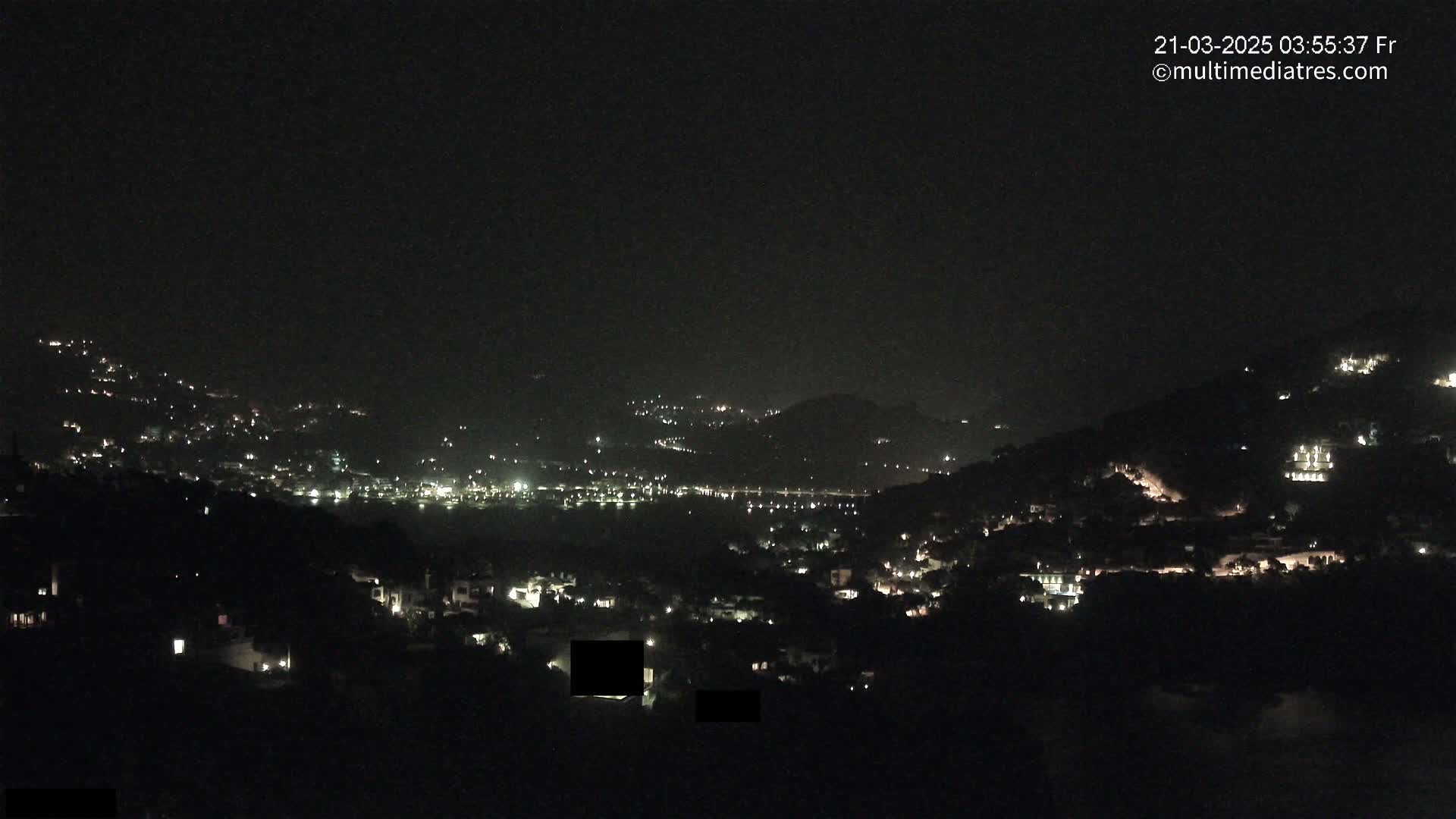 A nighttime view of a hilly town with scattered lights under a clear, dark sky.