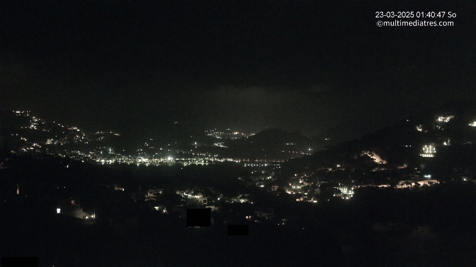 A nighttime view of a hillside town with scattered lights under a clear, dark sky.