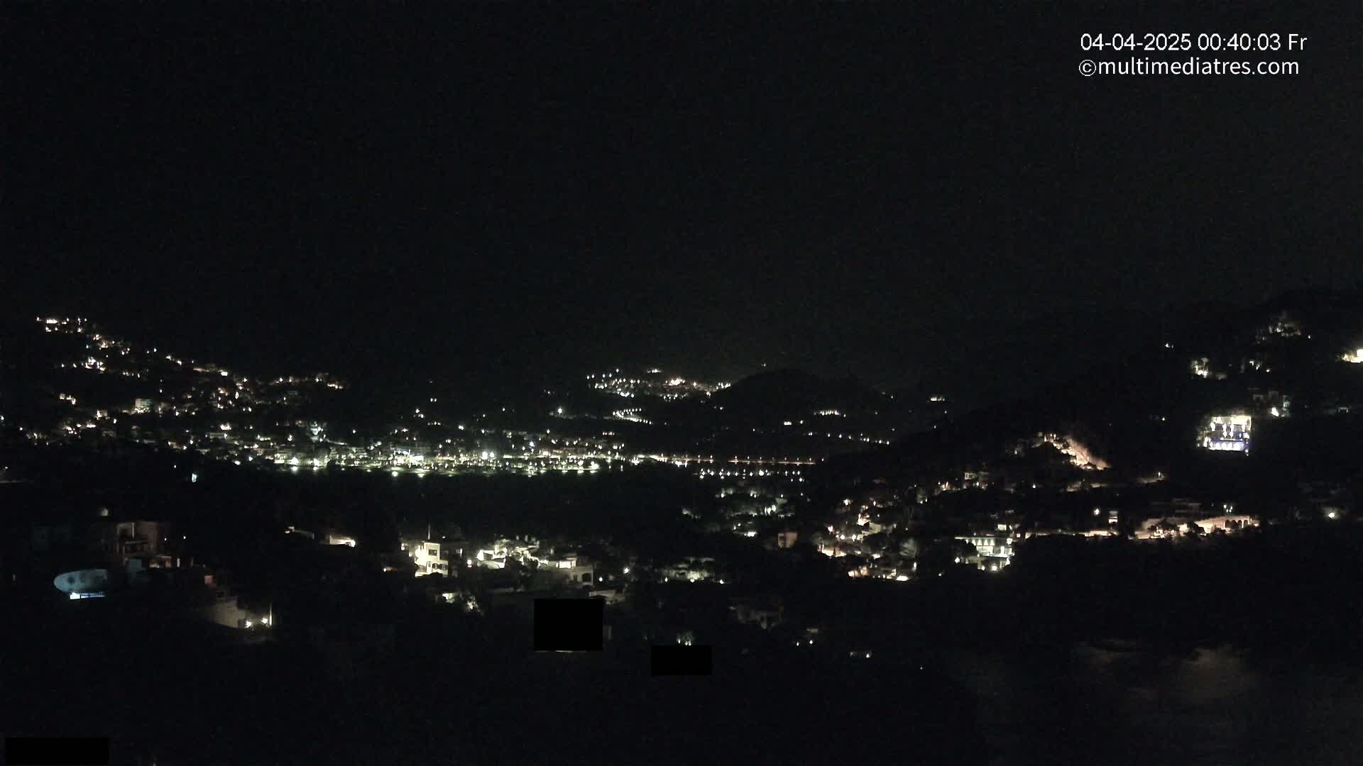 A nighttime view of a hillside town with many scattered lights under a clear, dark sky.