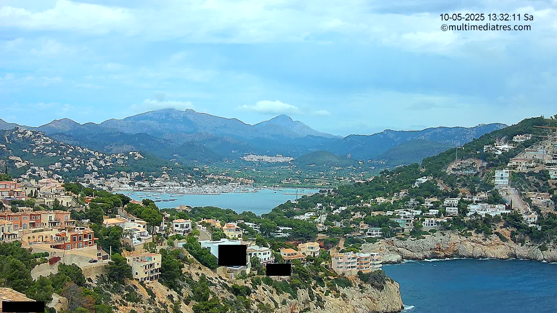 A coastal town nestled between a calm bay and mountains under a partly cloudy sky.